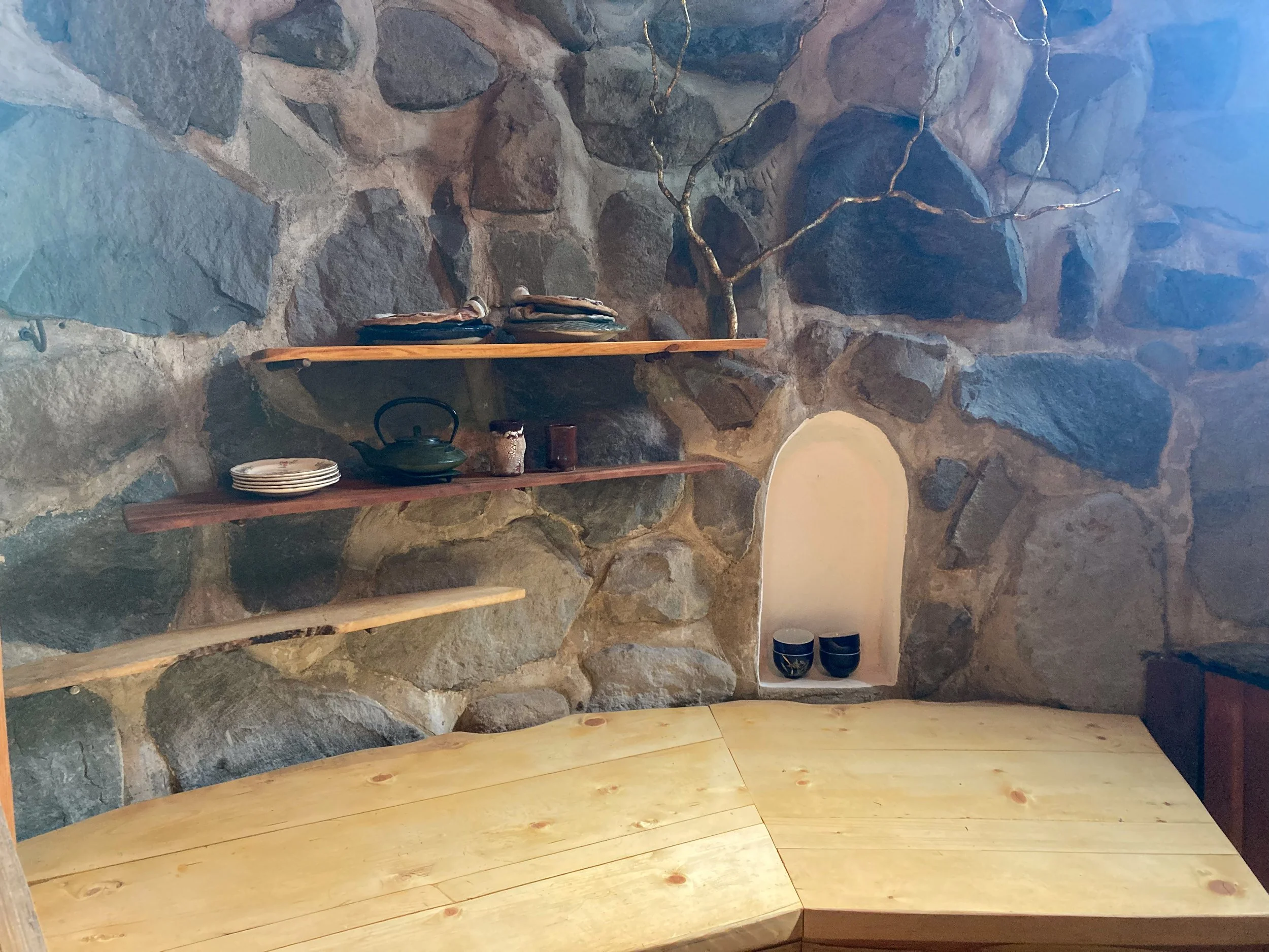 A wooden countertop, live edge shelves and arched cove in a stone building.