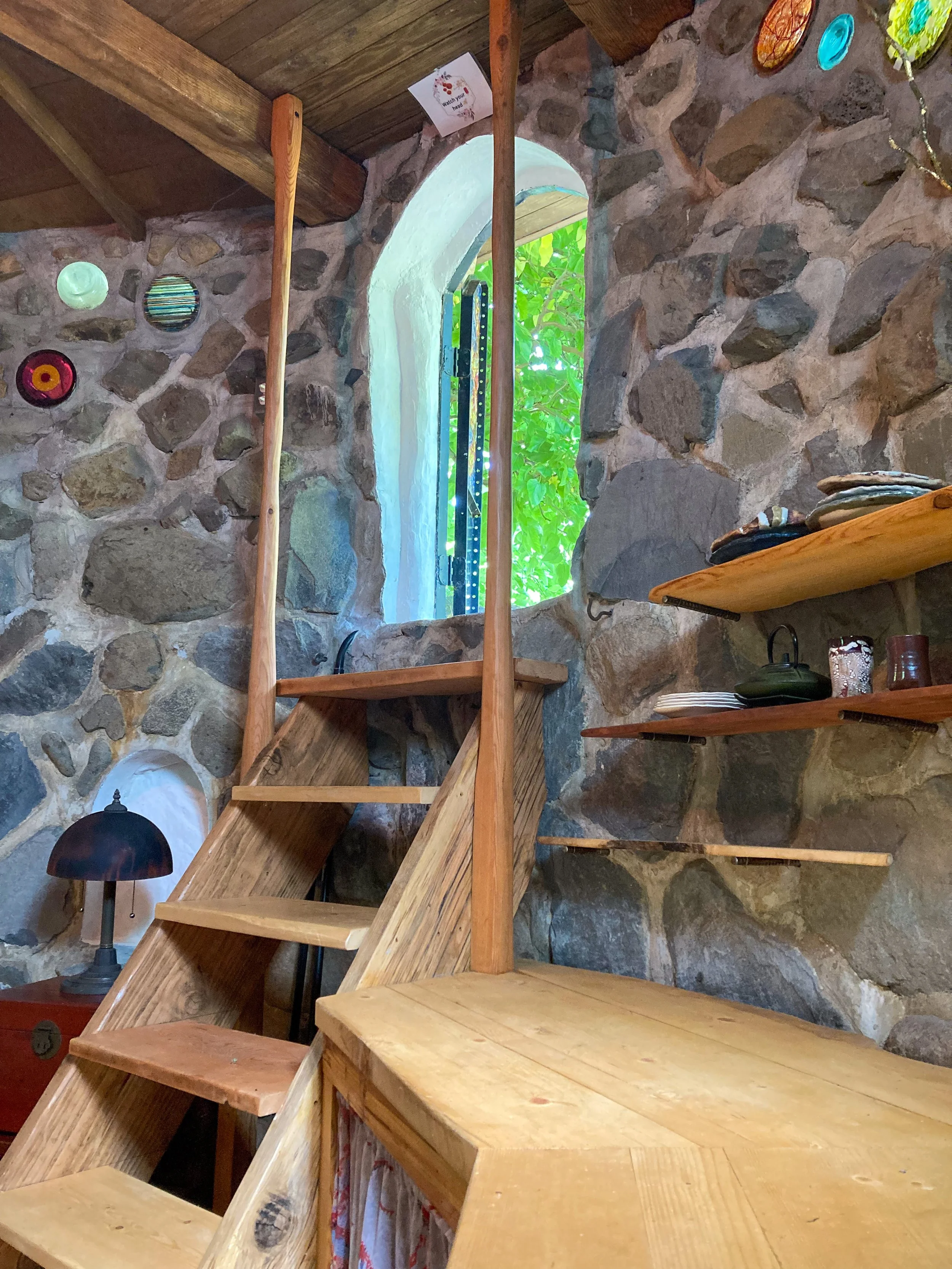 An interior wooden stairwell leading up to an arched doorway in a stone building.