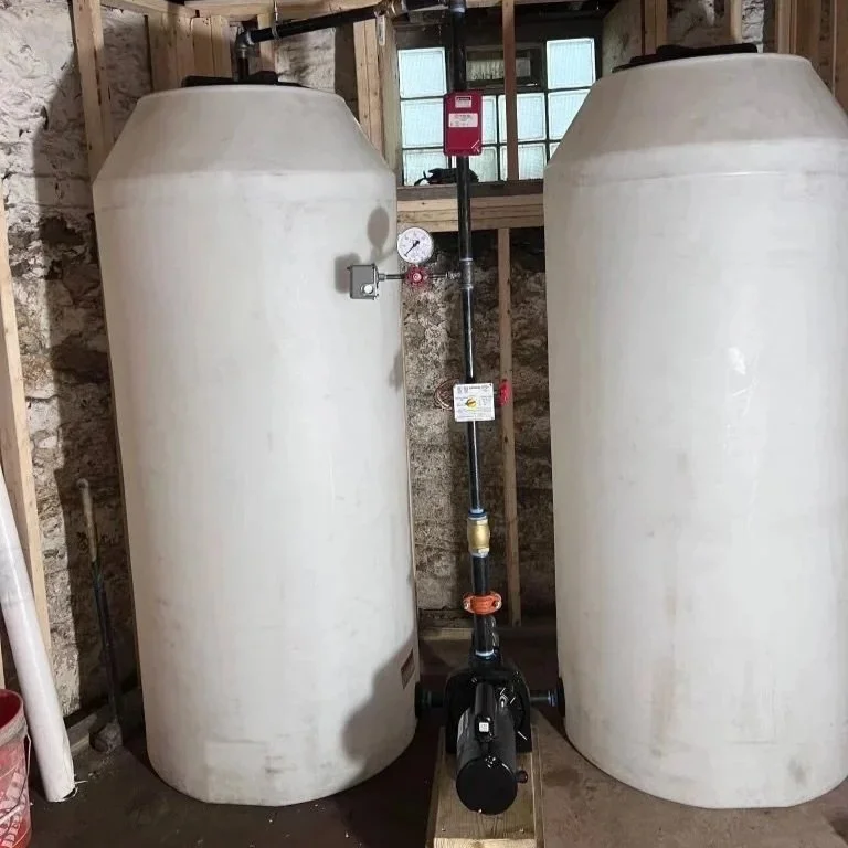 Two large white cylindrical tanks inside a building, with a black pipe and pump system between them.