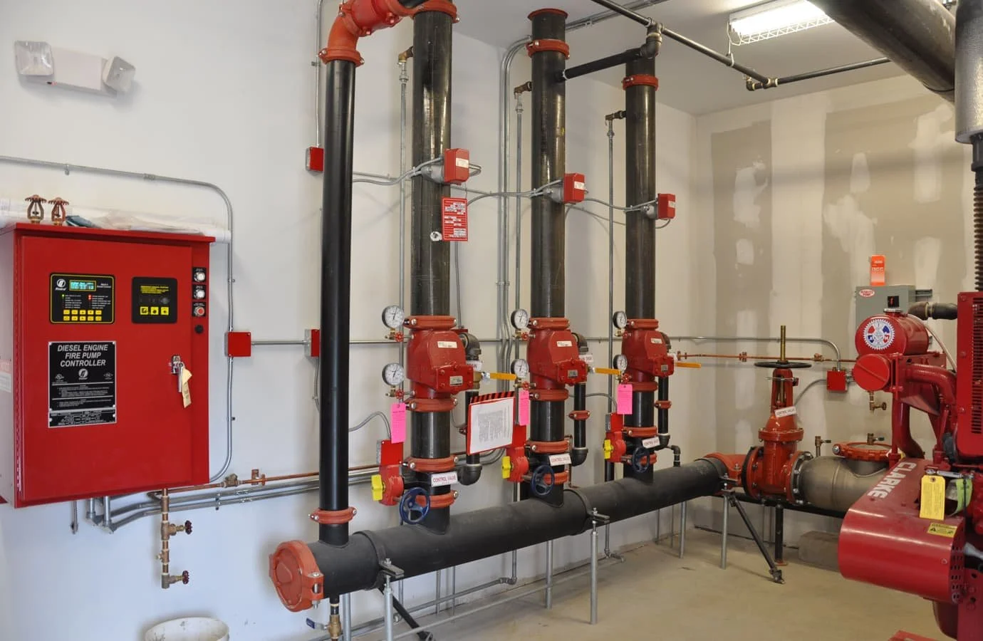 Fire pump room with black pipes, red fire control panel, gauges, and valves.