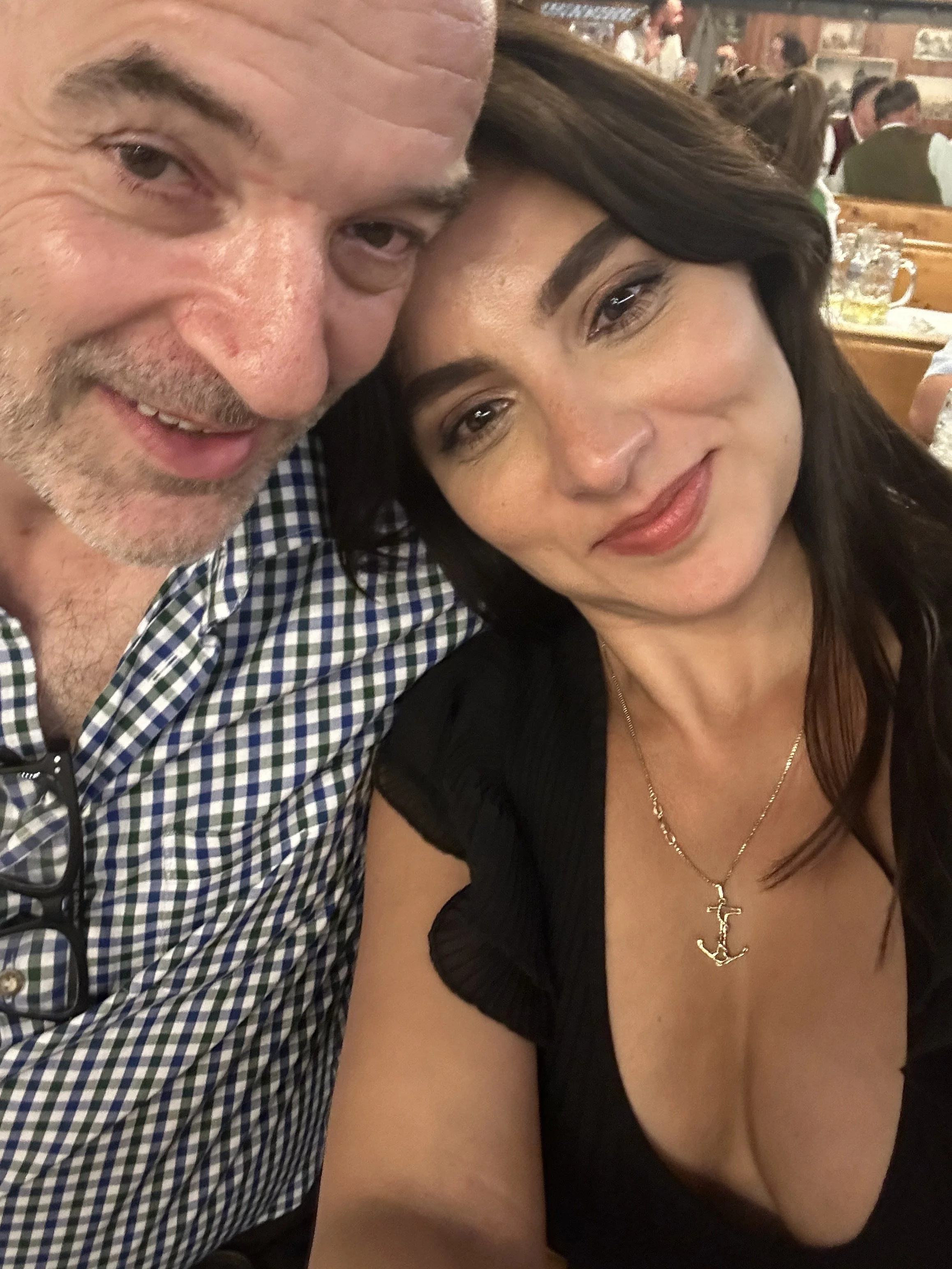 Close-up of a man and woman smiling at a restaurant, with people dining in the background.