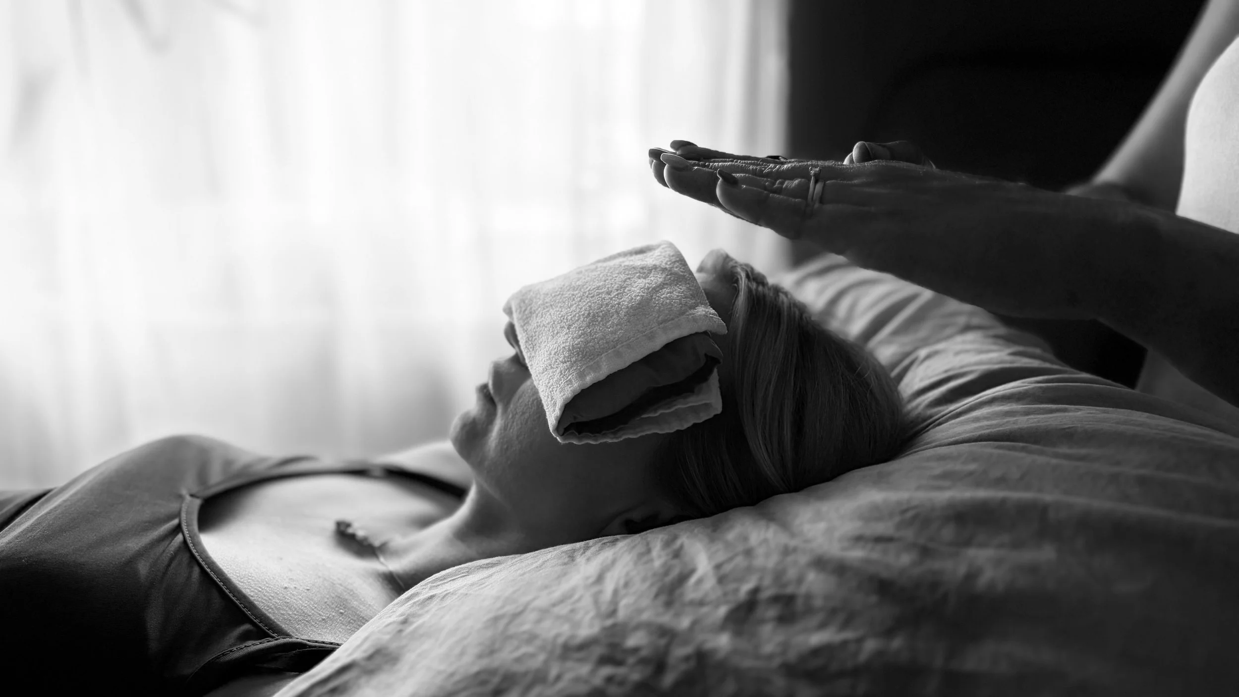 A person receiving a massage, lying face up with a towel over their face, in a monochrome photograph.