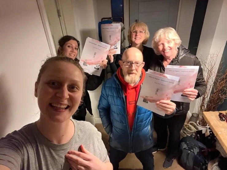 Group of five people indoors, holding Reiki certificates, smiling, celebrating an achievement.