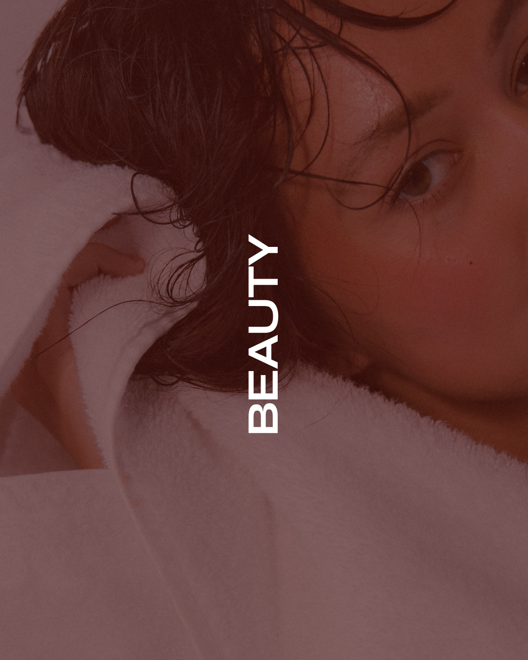 Close-up of a young woman with dark, wet hair lying on a white towel, with the word "BEAUTY" vertically overlaid in white text.