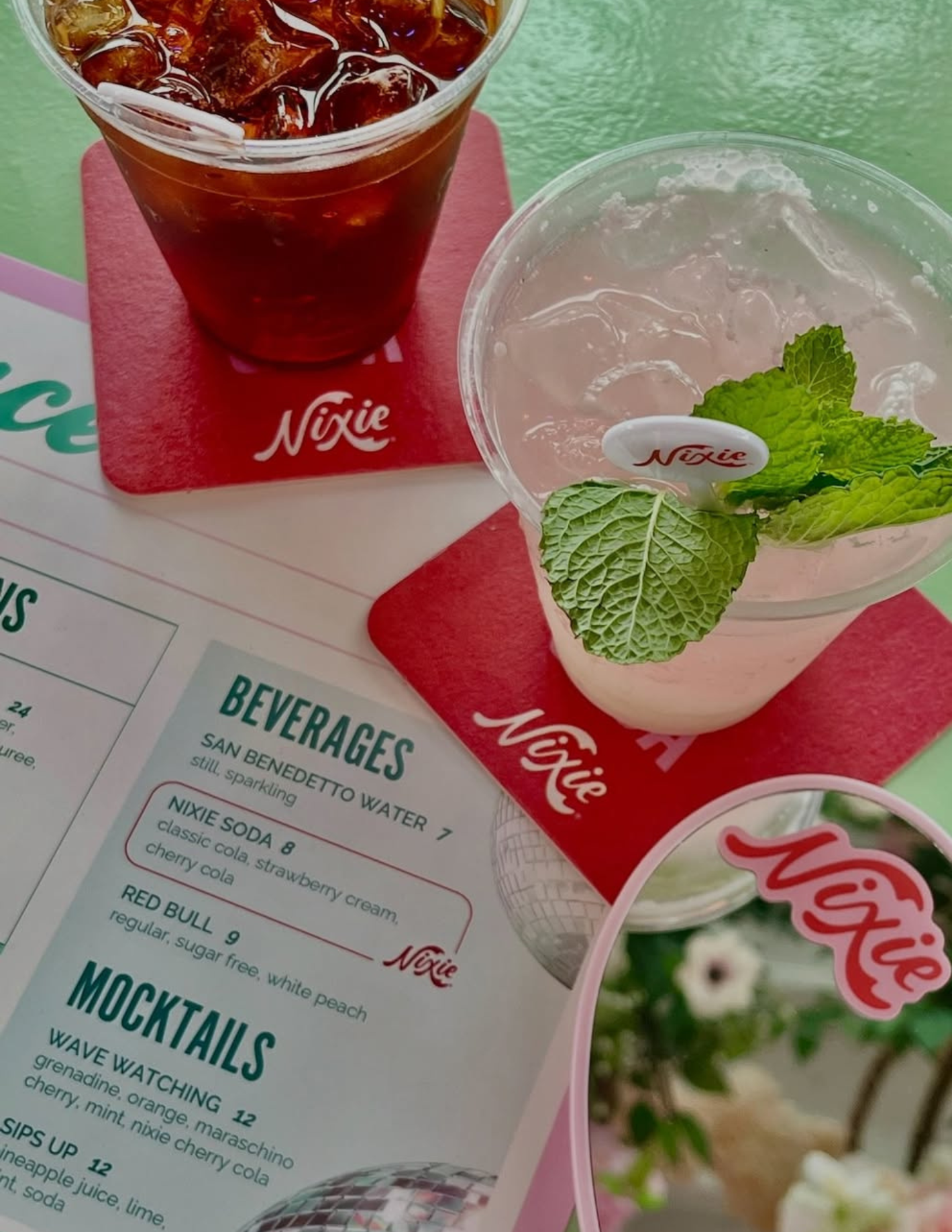 A menu with two drinks: a glass of iced cola and a cup of pink grapefruit cocktail garnished with mint leaves.