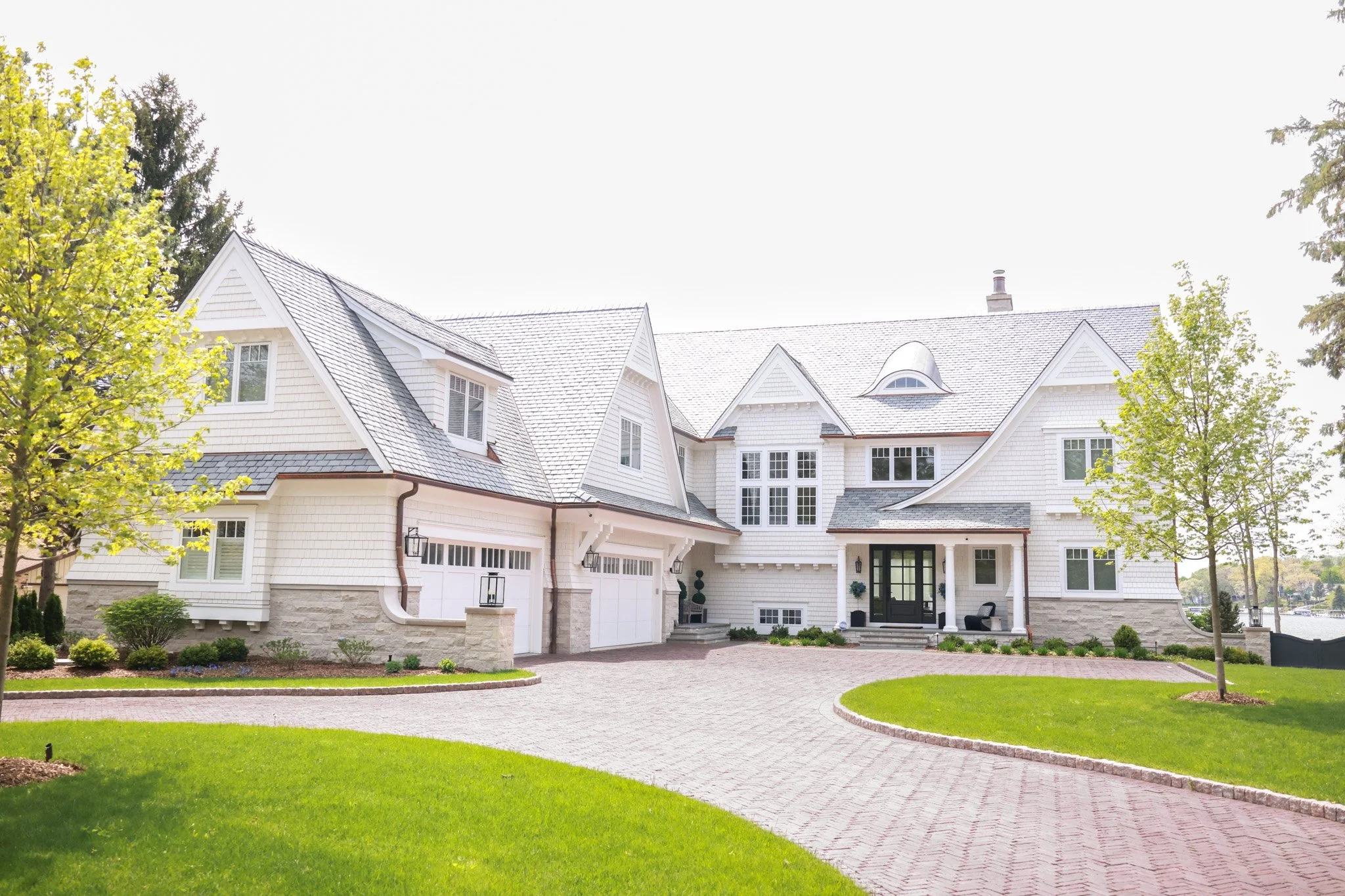 Front view of a large white house with a gray shingled roof, surrounded by green lawns and trees.