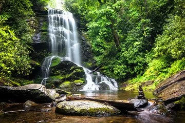 A scenic waterfall flowing over rocks into a calm pool surrounded by lush green trees.