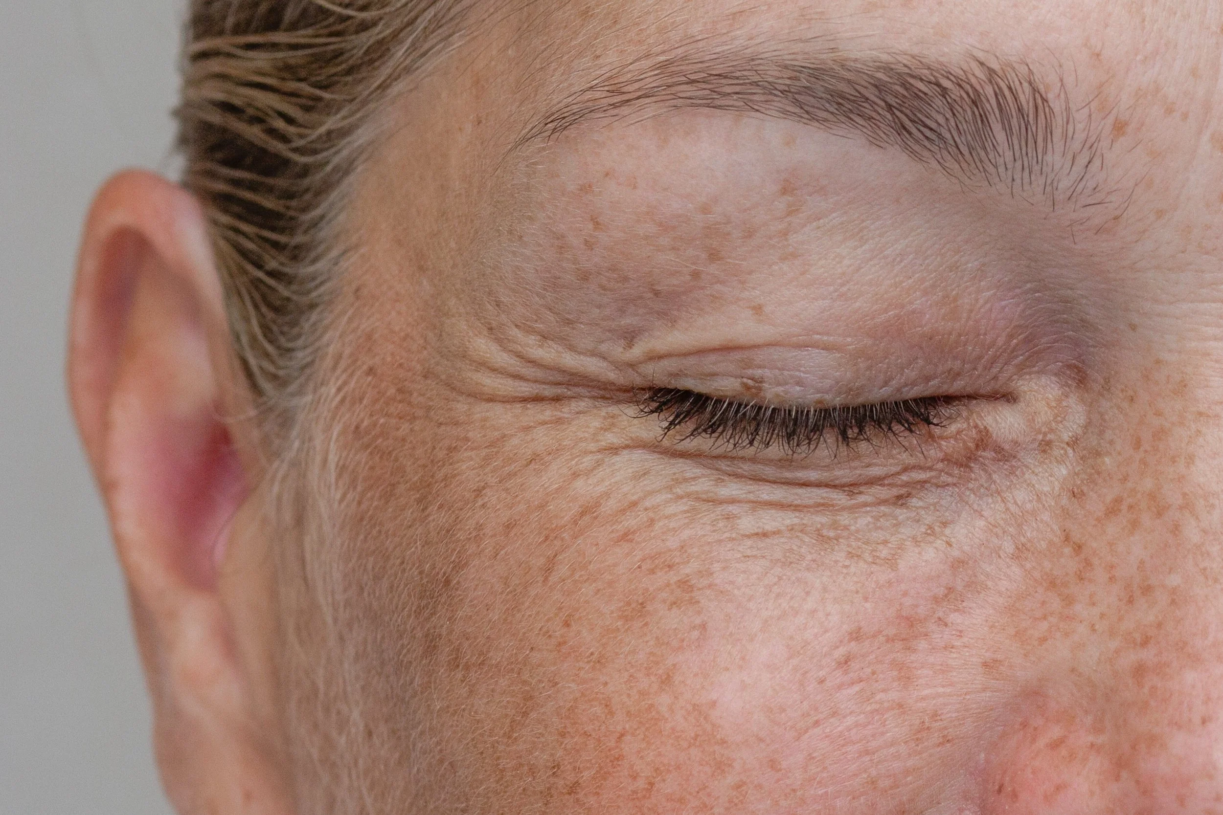 Close-up of a person's face with their eye closed, showing their eyebrow, eyelashes, and skin texture around the eye.