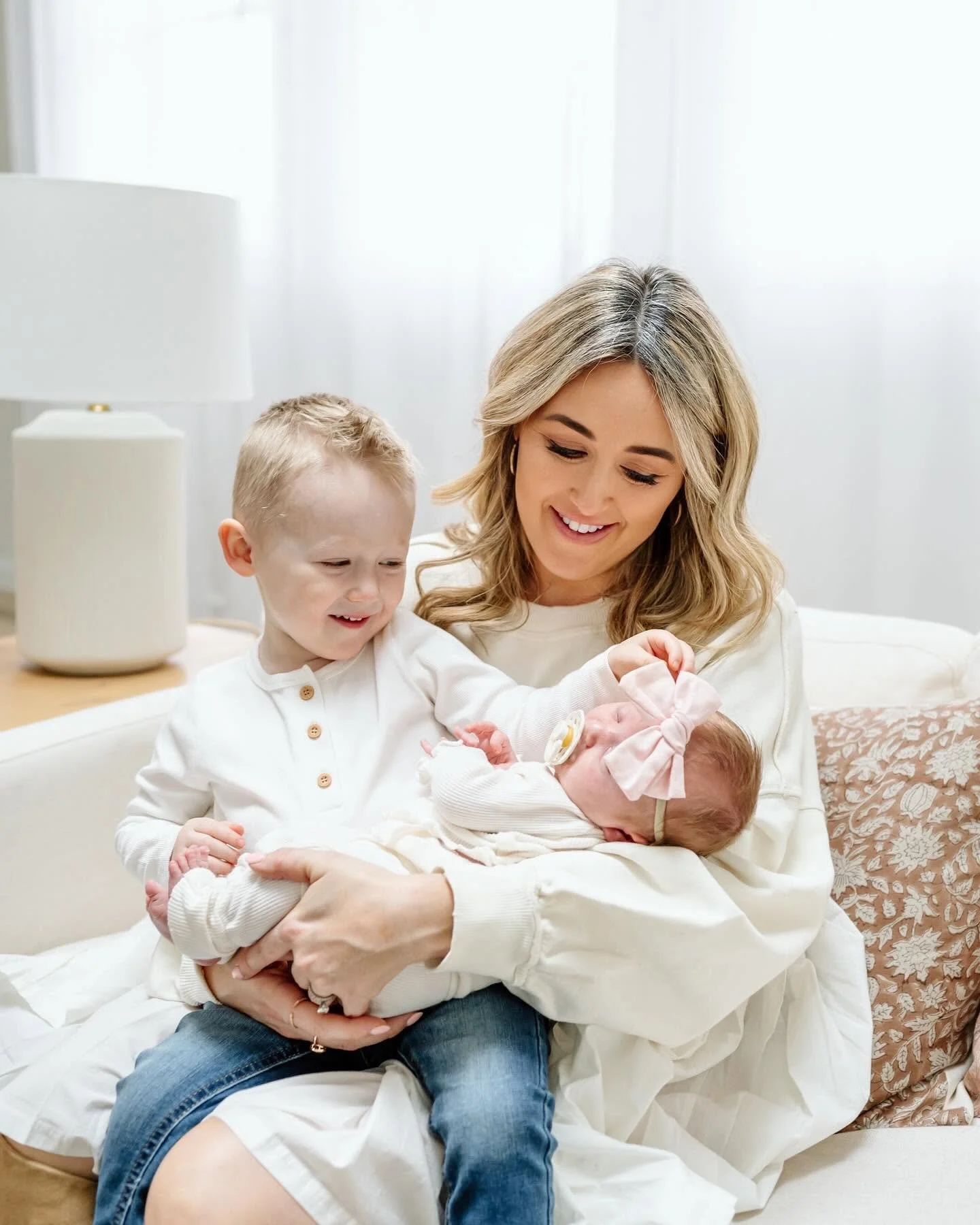 A woman holding a newborn baby surrounded by two young children in a cozy, well-lit room.