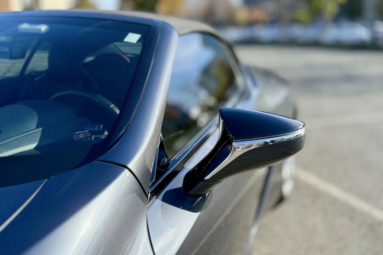 Close-up of a black side mirror on a silver Lexus convertible car in a parking lot.