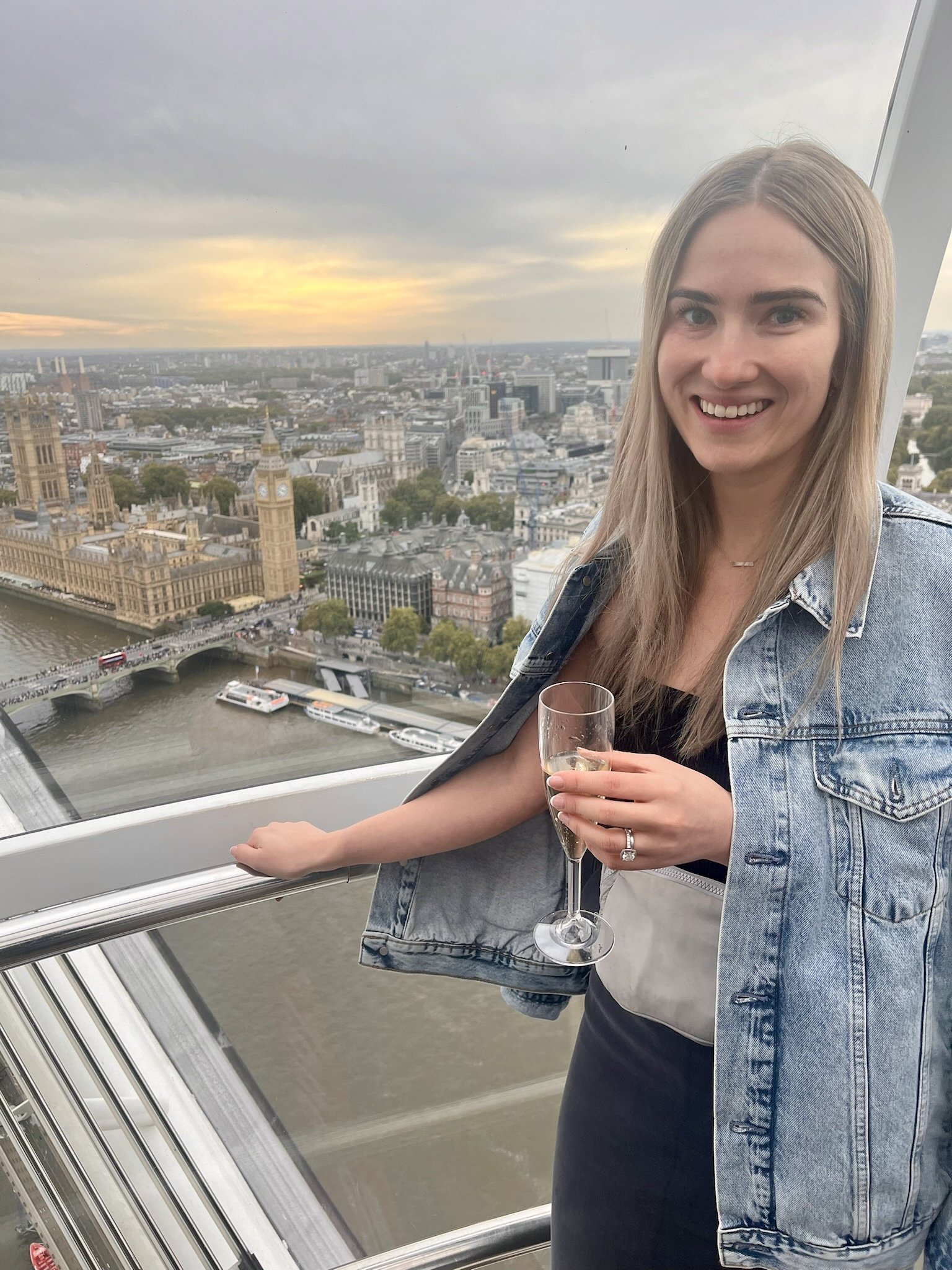 woman smiling on London's Ferris wheel, Big Ben and the Houses of Parliament visible below, holding a glass of champagne