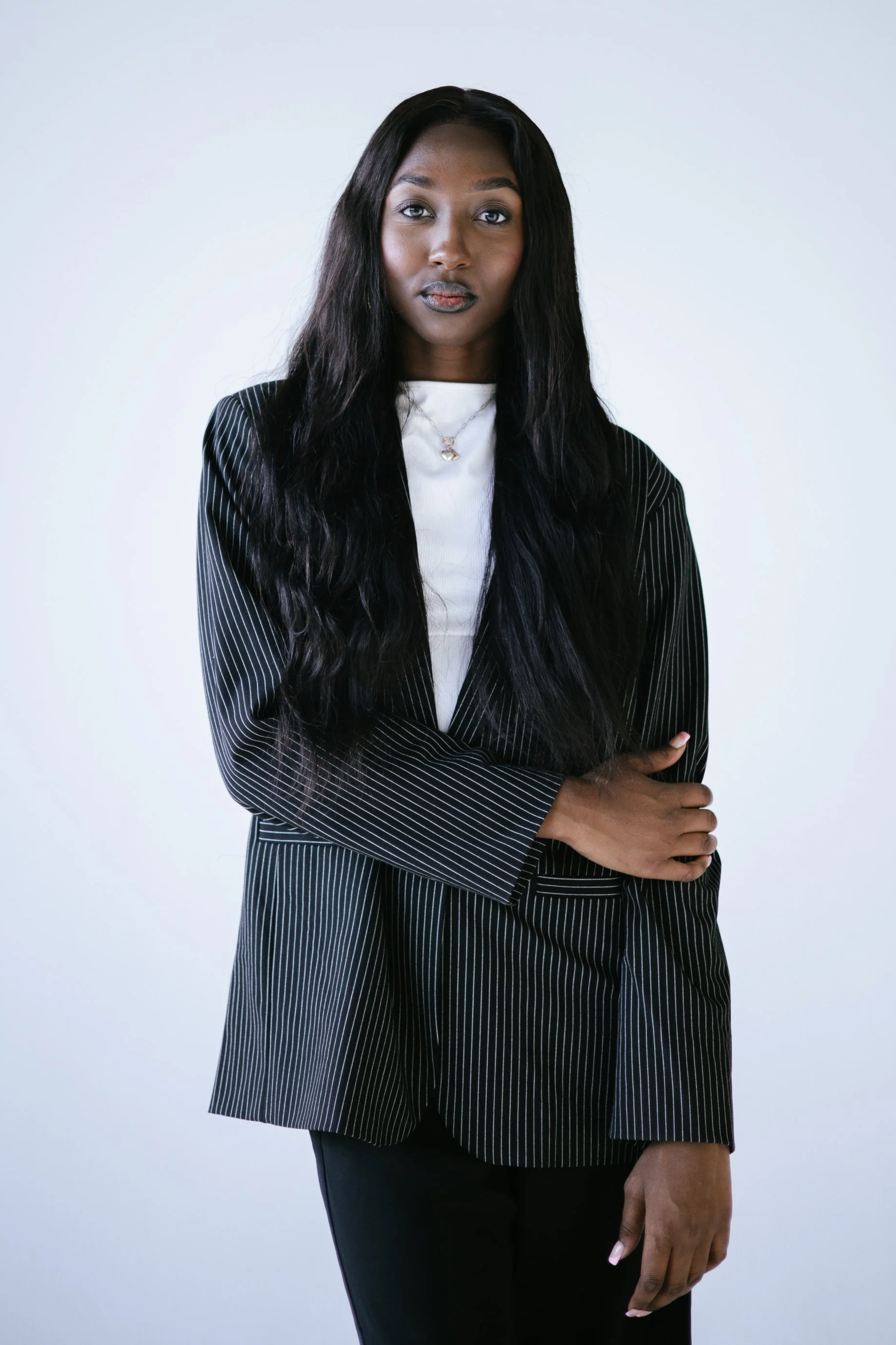 A woman with long dark hair, wearing a striped blazer over a white top, posing against a plain light gray background.