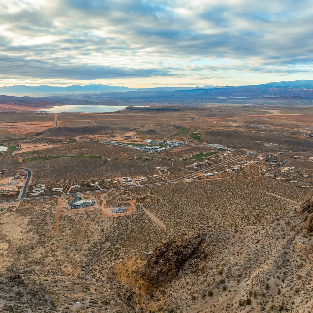 Aerial view of a desert landscape with a large lake in the distance, mountains, and scattered buildings and roads.