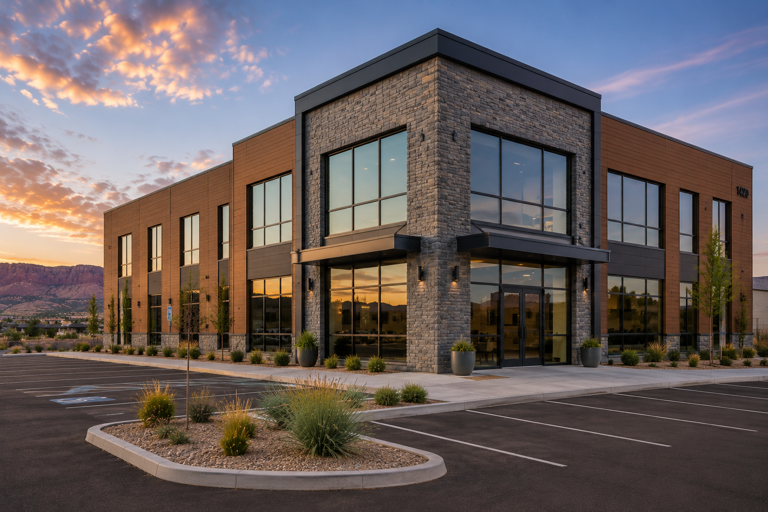 Modern office building with large glass windows, stone and wood exterior, landscaped parking lot at sunset