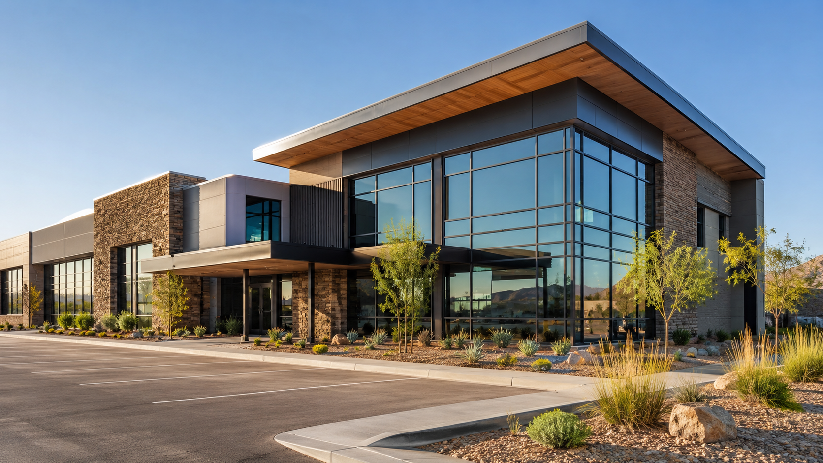 Modern commercial building with large glass windows, stone accents, and desert landscaping in front.