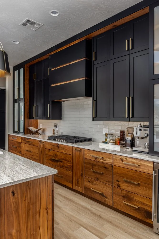 Modern kitchen with black upper cabinets, wooden lower cabinets, a white subway tile backsplash, and a granite countertop with a coffee maker and other small appliances.