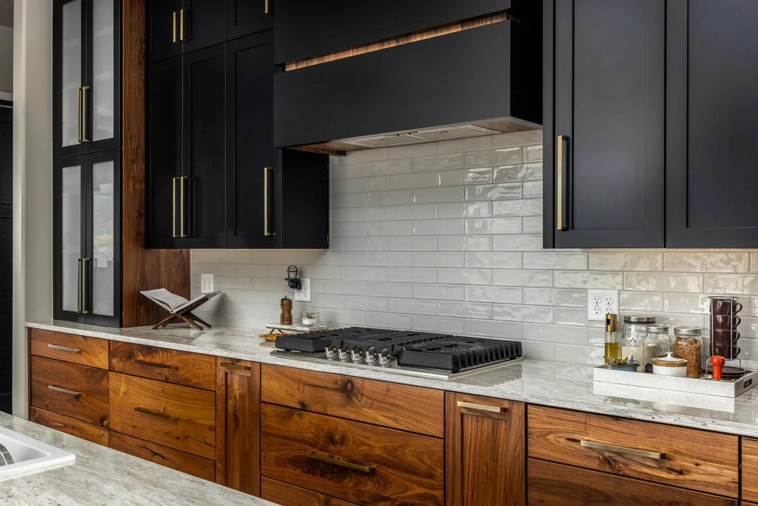 Modern kitchen with black upper cabinets, wooden lower cabinets, white tile backsplash, and a stove with a range hood.