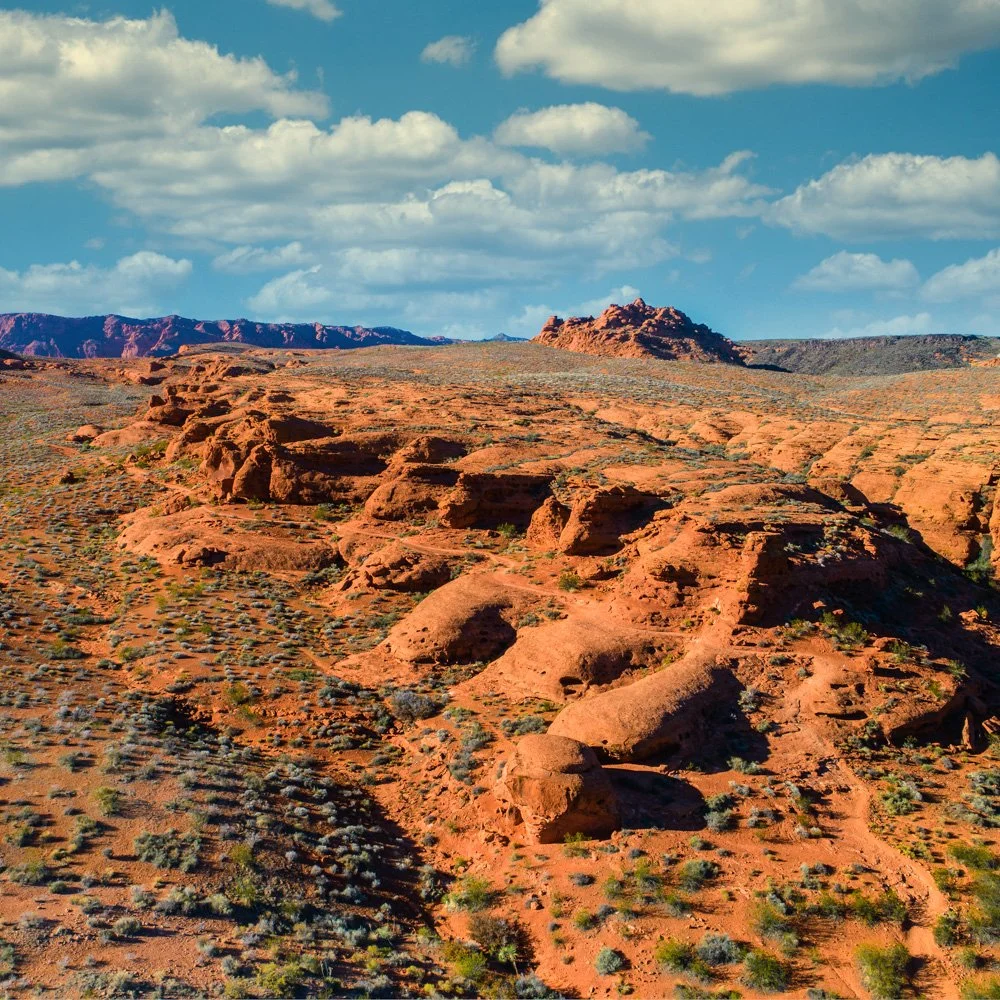 Red rock formations and desert landscape under a blue sky with clouds.
