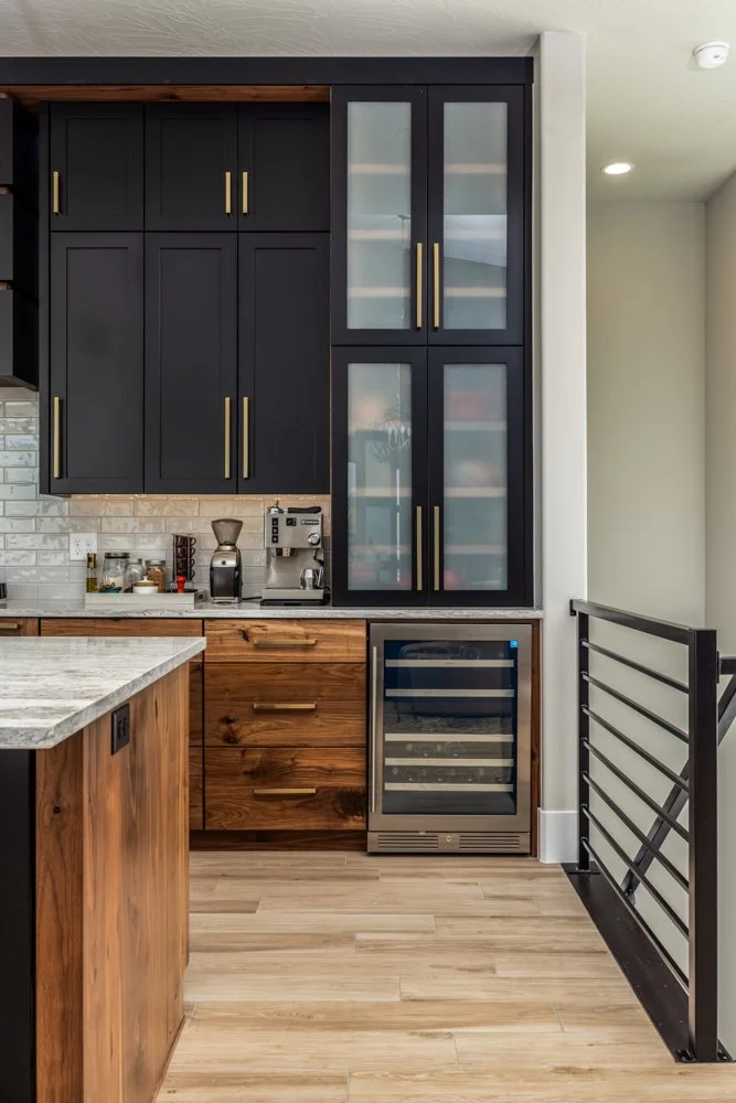 Modern kitchen with black upper cabinets, glass-front upper cabinets, wooden lower cabinets, a built-in wine cooler, and a countertop coffee station.