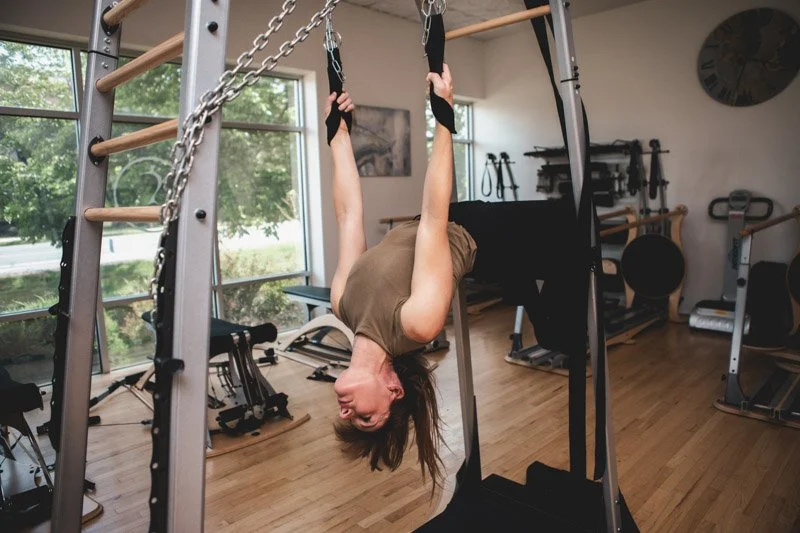 Leah is doing a bridging motion with her head back and spine arched, assisted by pulleys on the GYROTONIC Archway equipment.