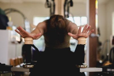 Leah is folding forward with her hands outstretched on the handles of a wood and black GYROTONICs frame.