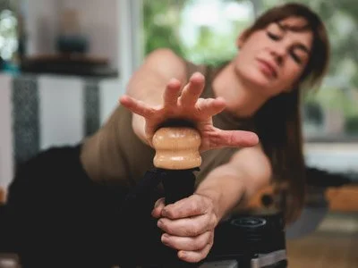 Leah is sitting on a bench with her torso reaching forward towards a wooden handle. Her hands grab the handle as her head and spine rotate.