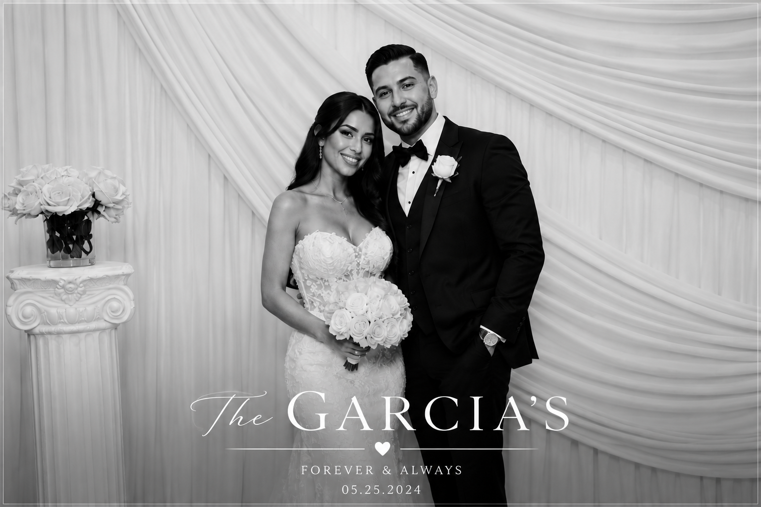 Black and white photo of a bride and groom standing together at their wedding, with the bride holding a bouquet of roses and the groom wearing a tuxedo with a white rose boutonniere, against a backdrop of draped fabric.