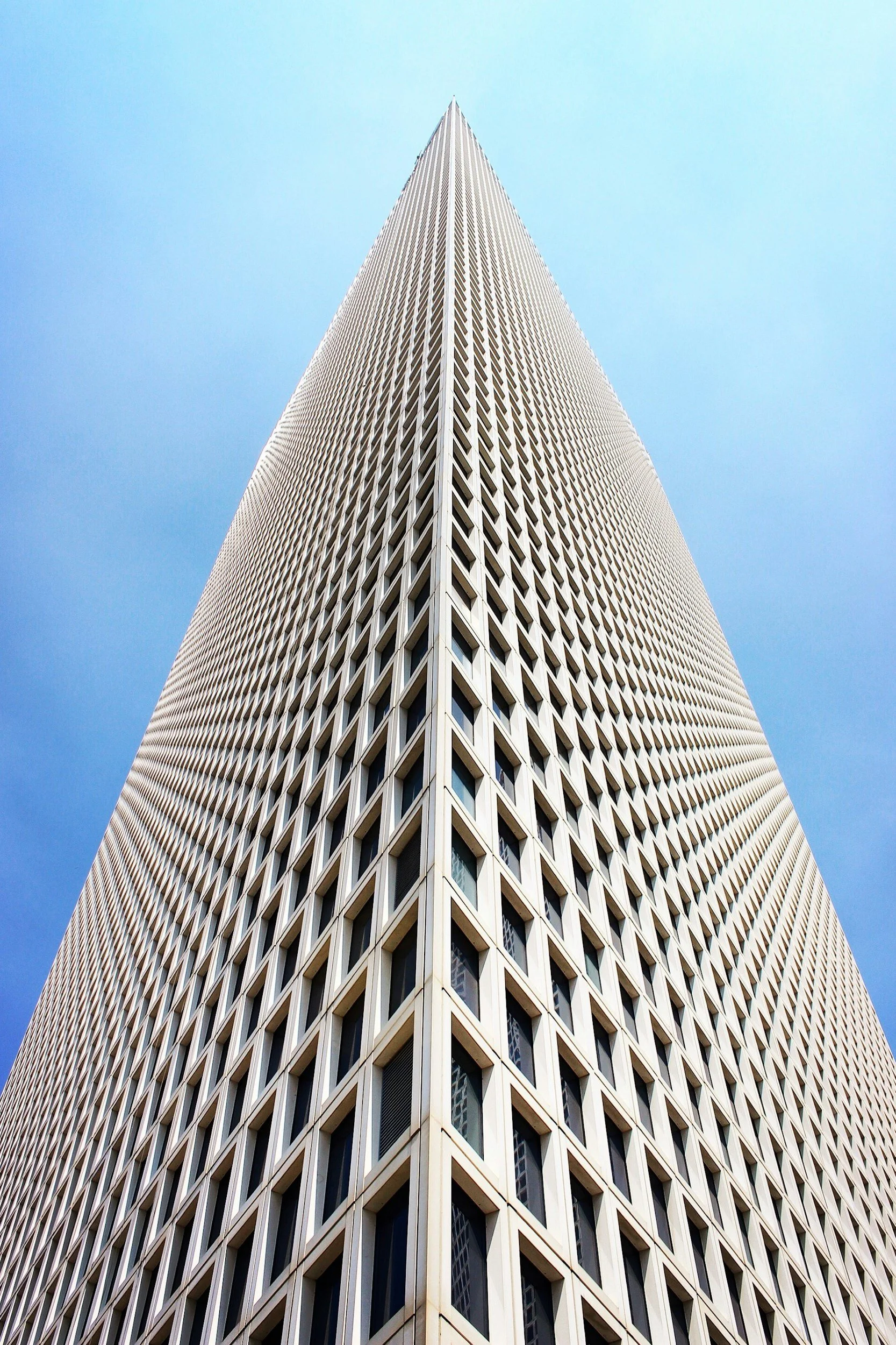 The photo shows the upward view of a tall, modern skyscraper with a grid-like pattern on its facade and a clear blue sky in the background.
