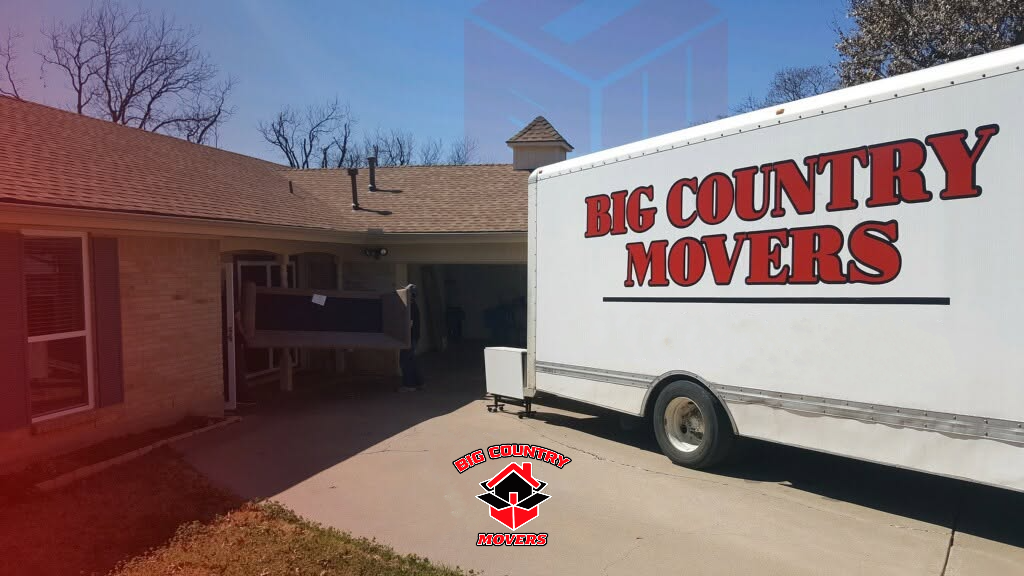 A moving truck with the company name "Big Country Movers" parked in front of a house, with a piece of furniture being carried into the house.