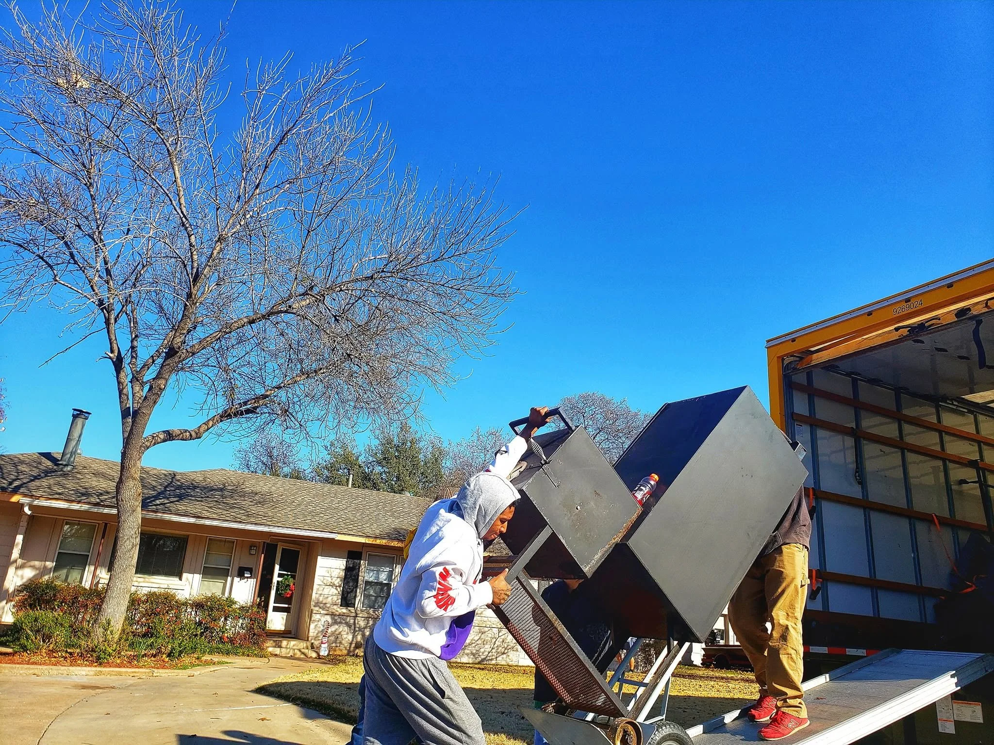 Two workers are installing an HVAC unit onto the side of a house, one is working inside the truck and the other is holding the HVAC unit.