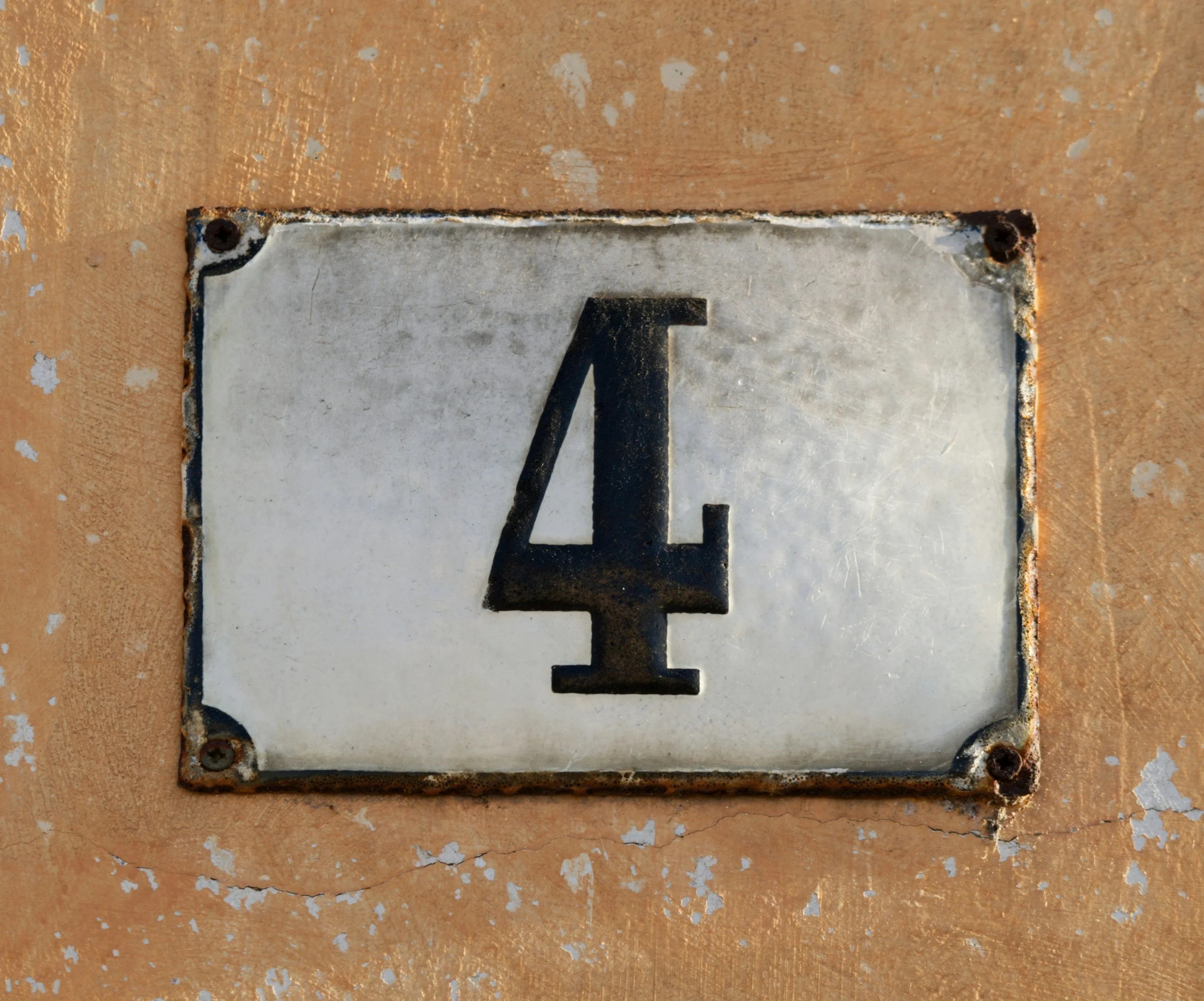 Close-up of a metallic house number plaque with the number 2 attached to a weathered, rusty wall.
