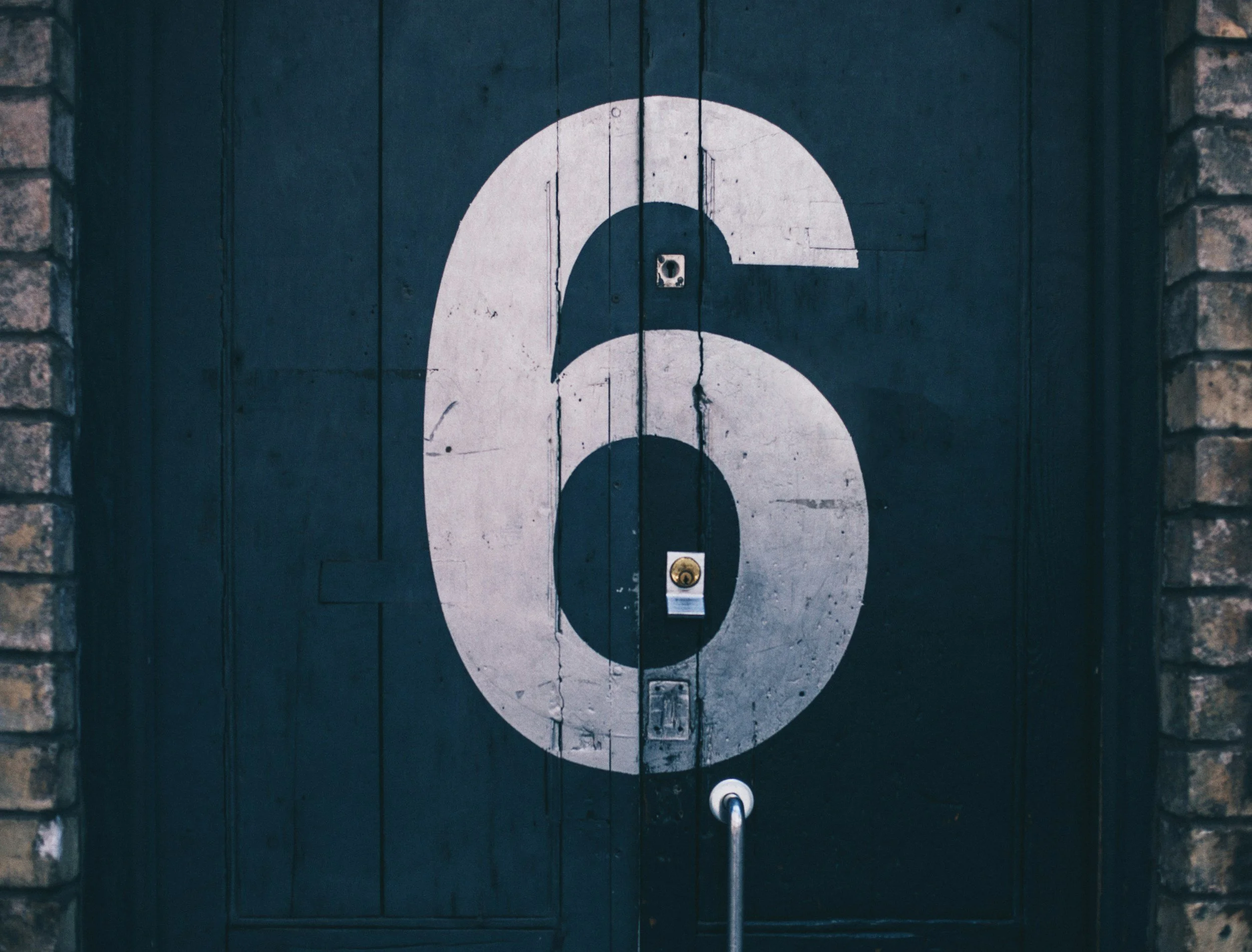 A white painted number 3 on a dark wooden door, with brick walls on either side.