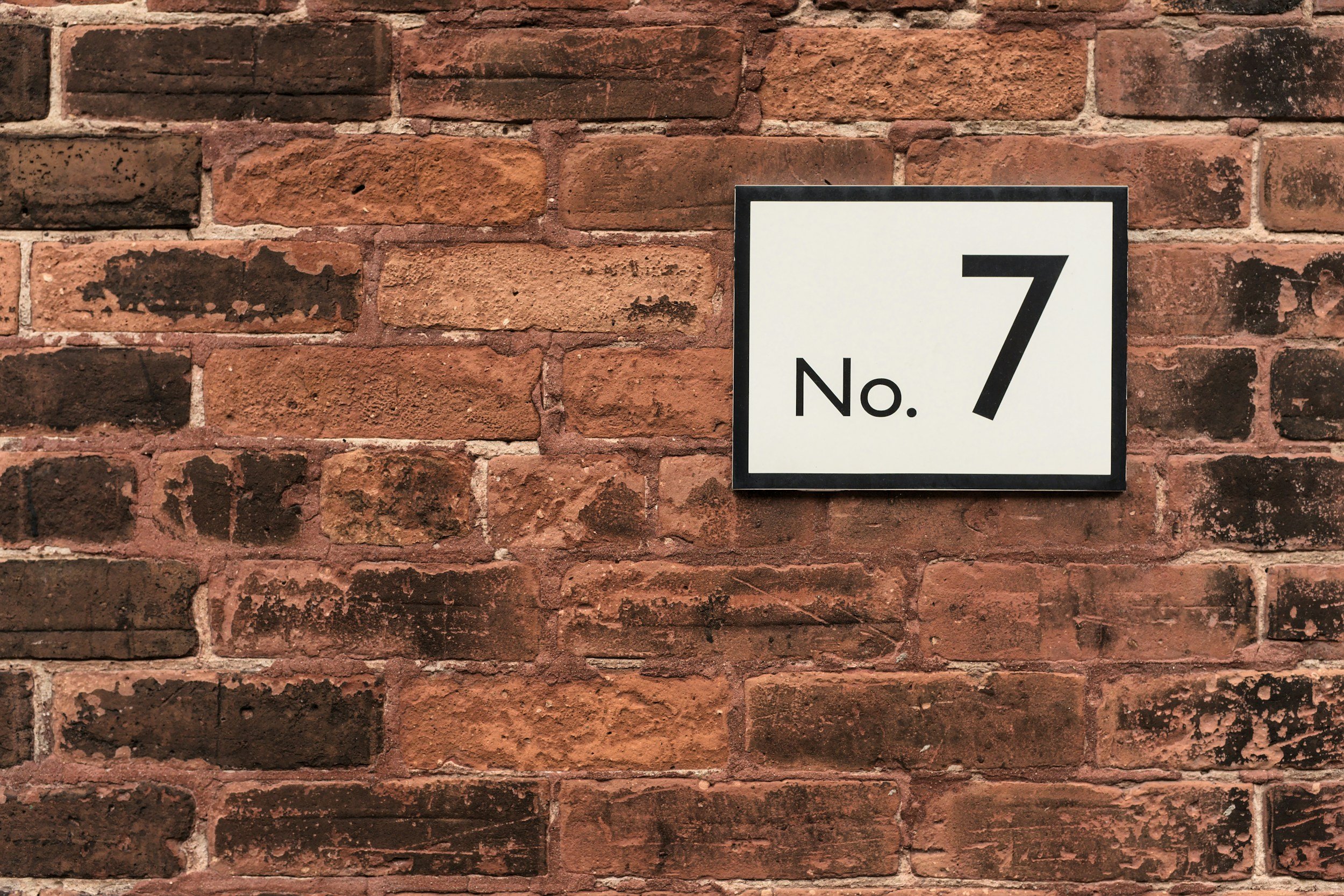 A brick wall with a white sign displaying the number 7 and the word No.