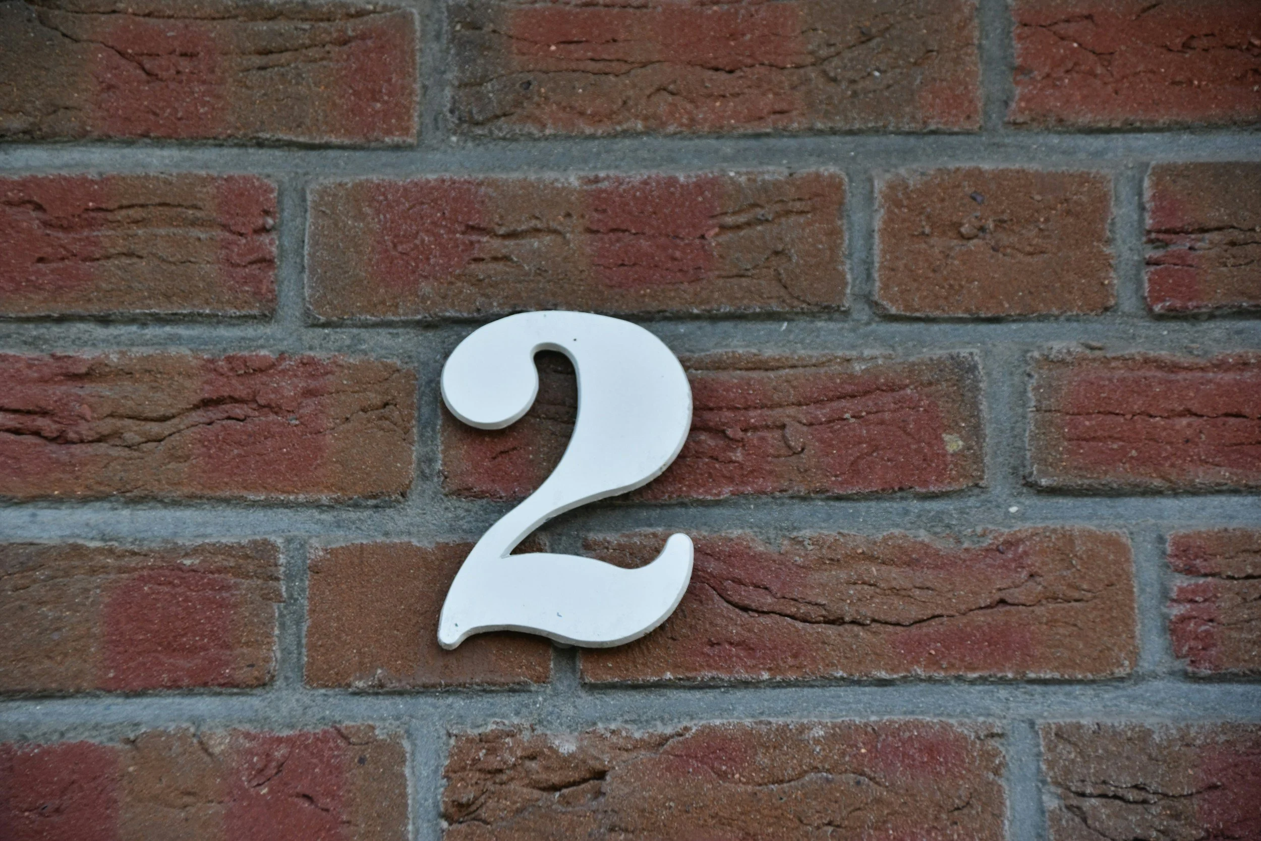 Close-up of a white question mark sign mounted on a red brick wall.