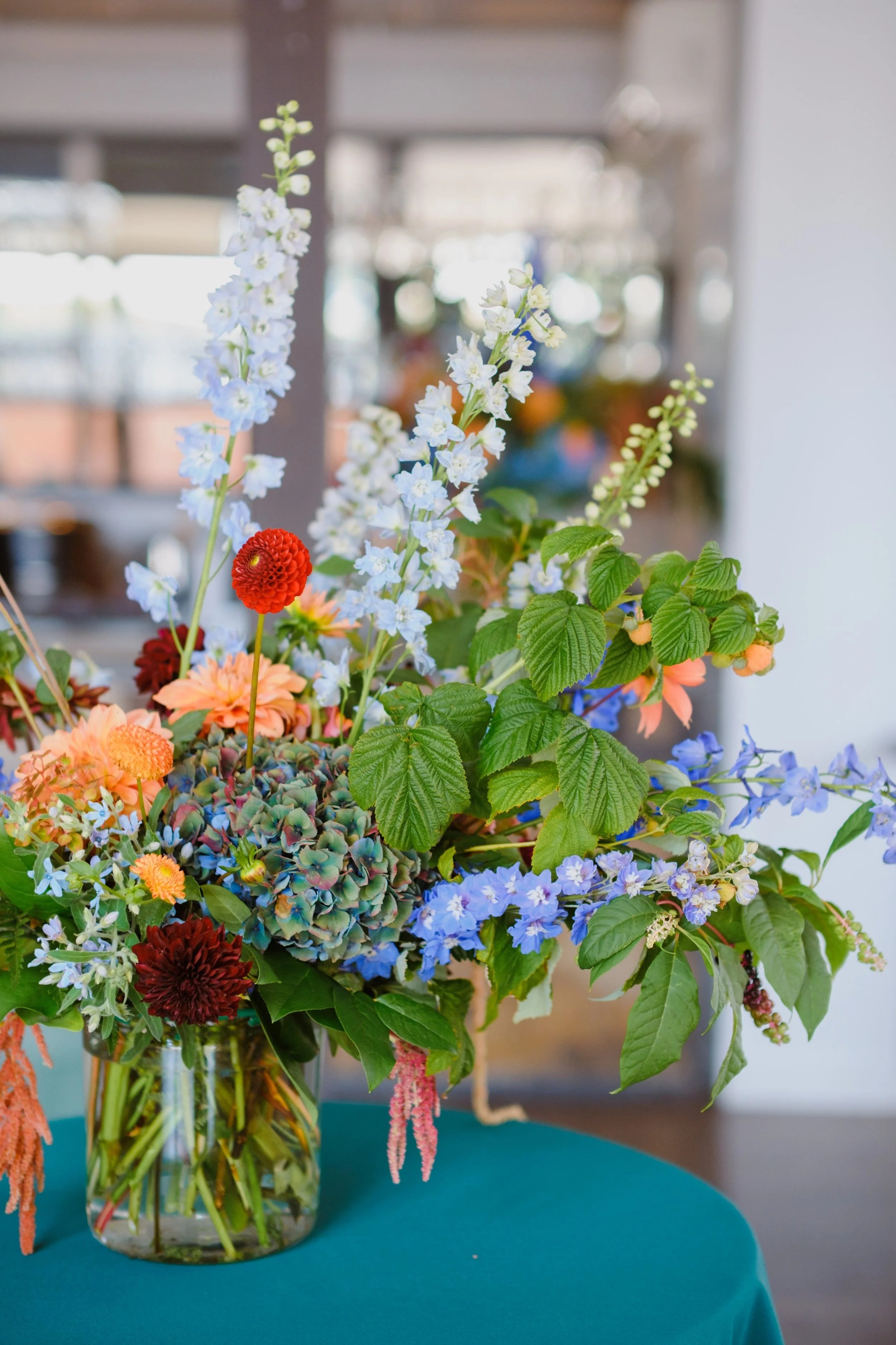 A colorful flower bouquet with blue, orange, and burgundy flowers on a green table, at Fremont Foundry
