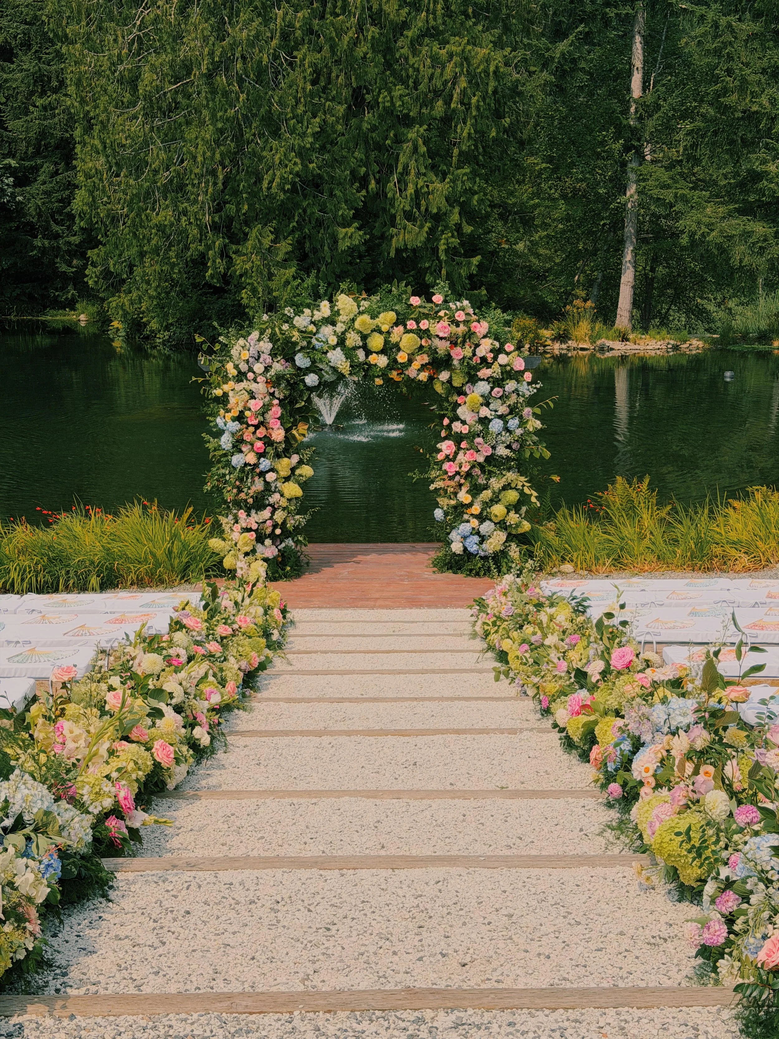 A floral wedding arch set up over a pond with lush green trees in the background.