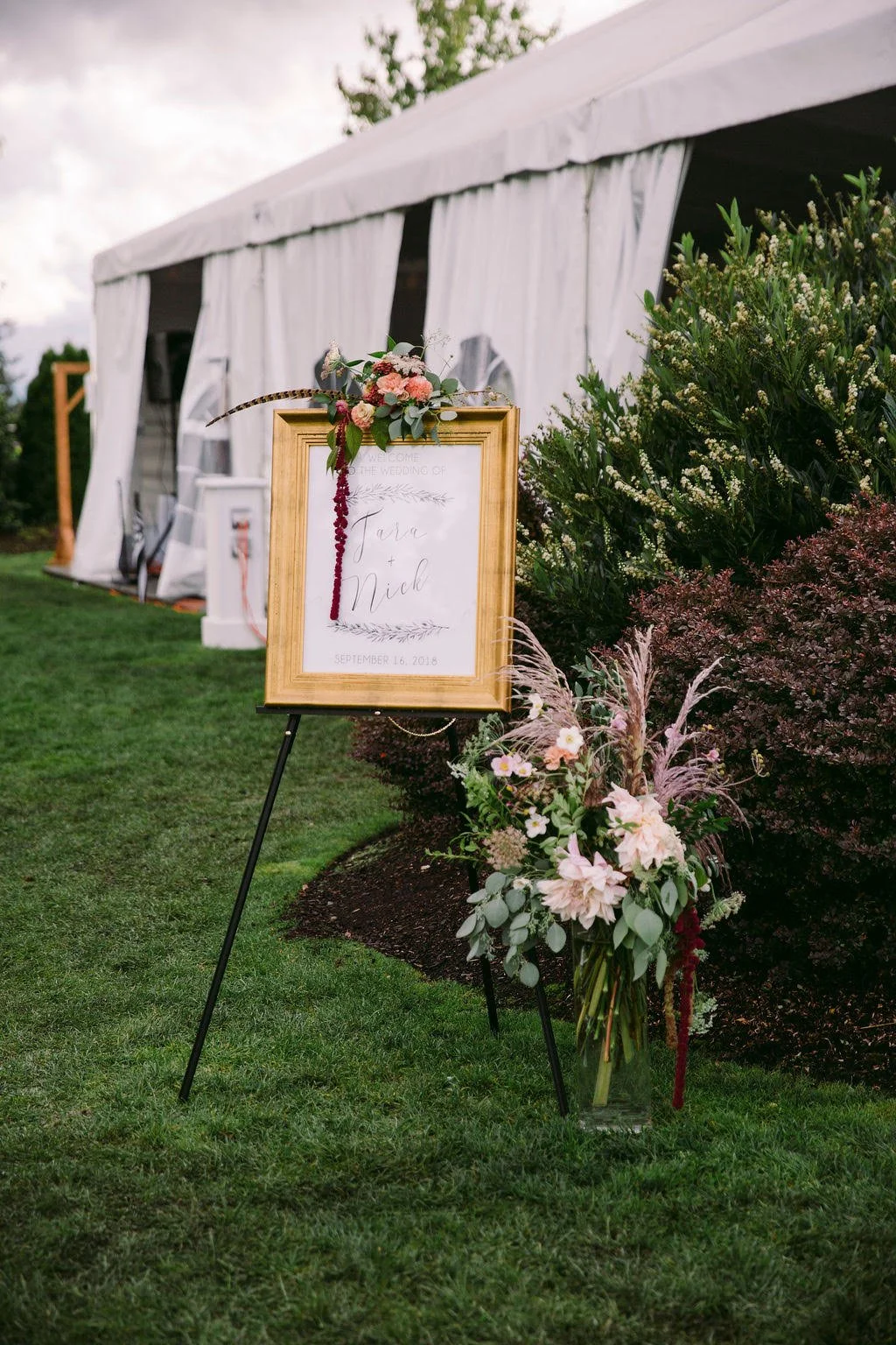 Wedding reception sign with floral decorations outside a white tent.