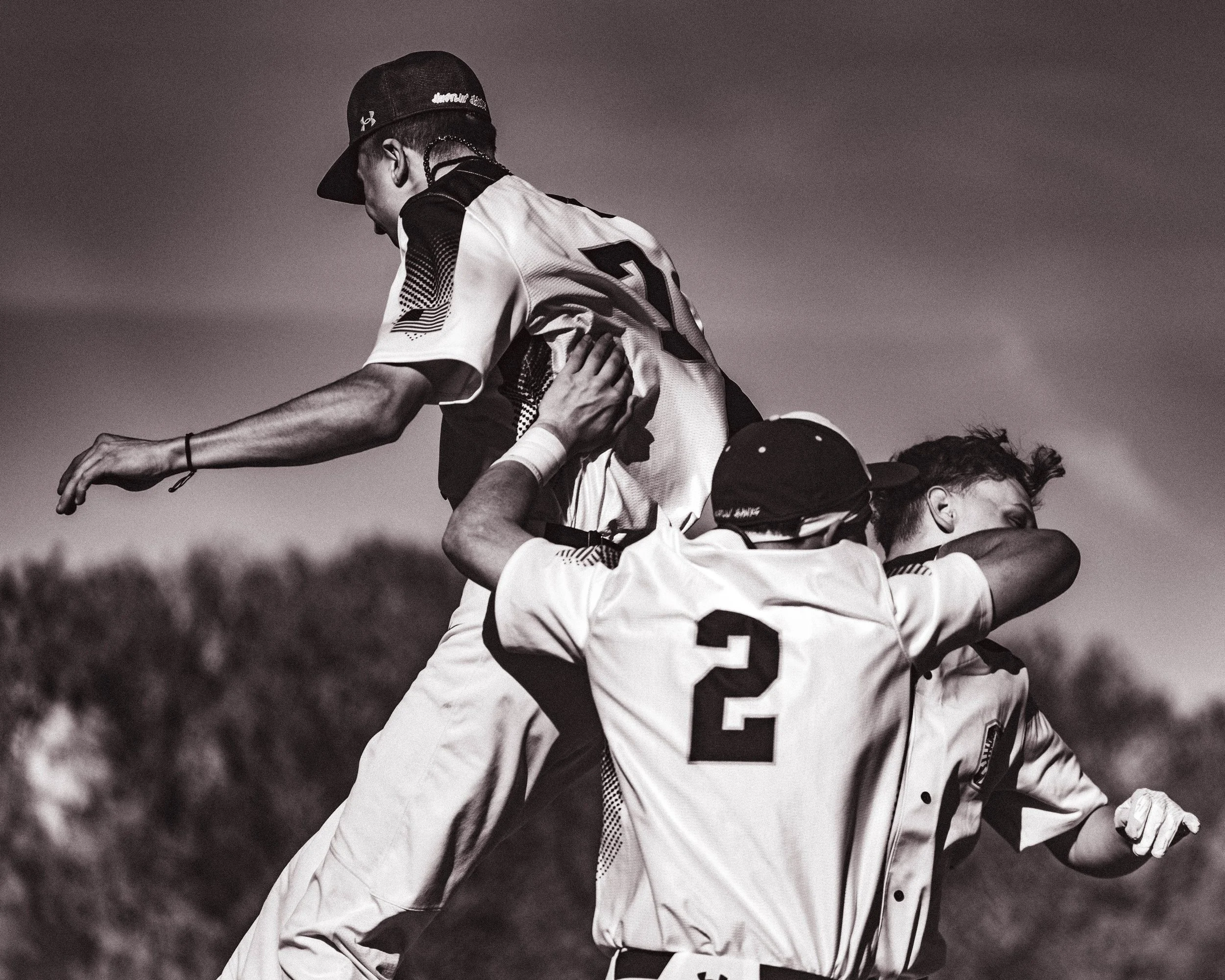 Black and white photo of baseball players celebrating on the field, one player being lifted by teammates, cheering.