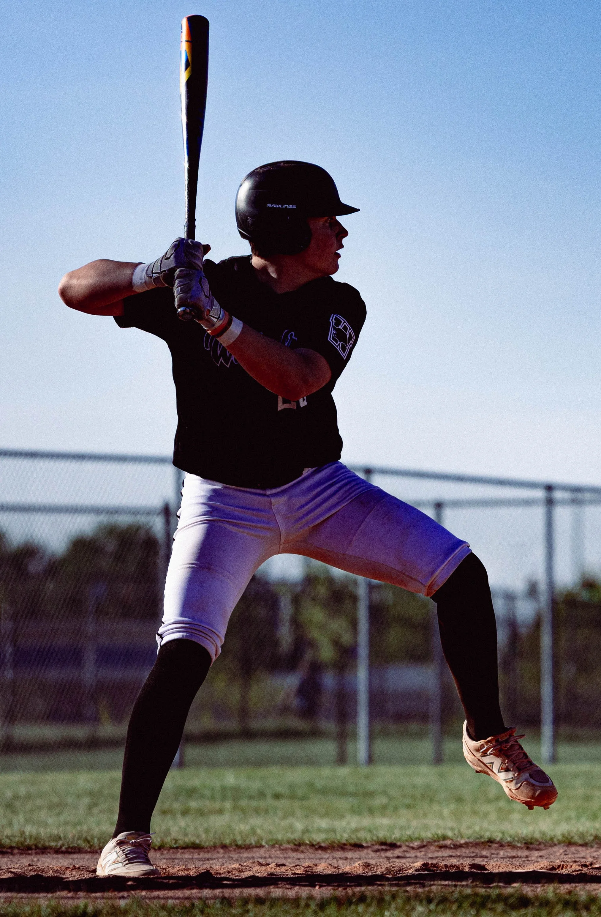 A baseball player in black and white uniform preparing to hit the ball at a baseball field during sunset.