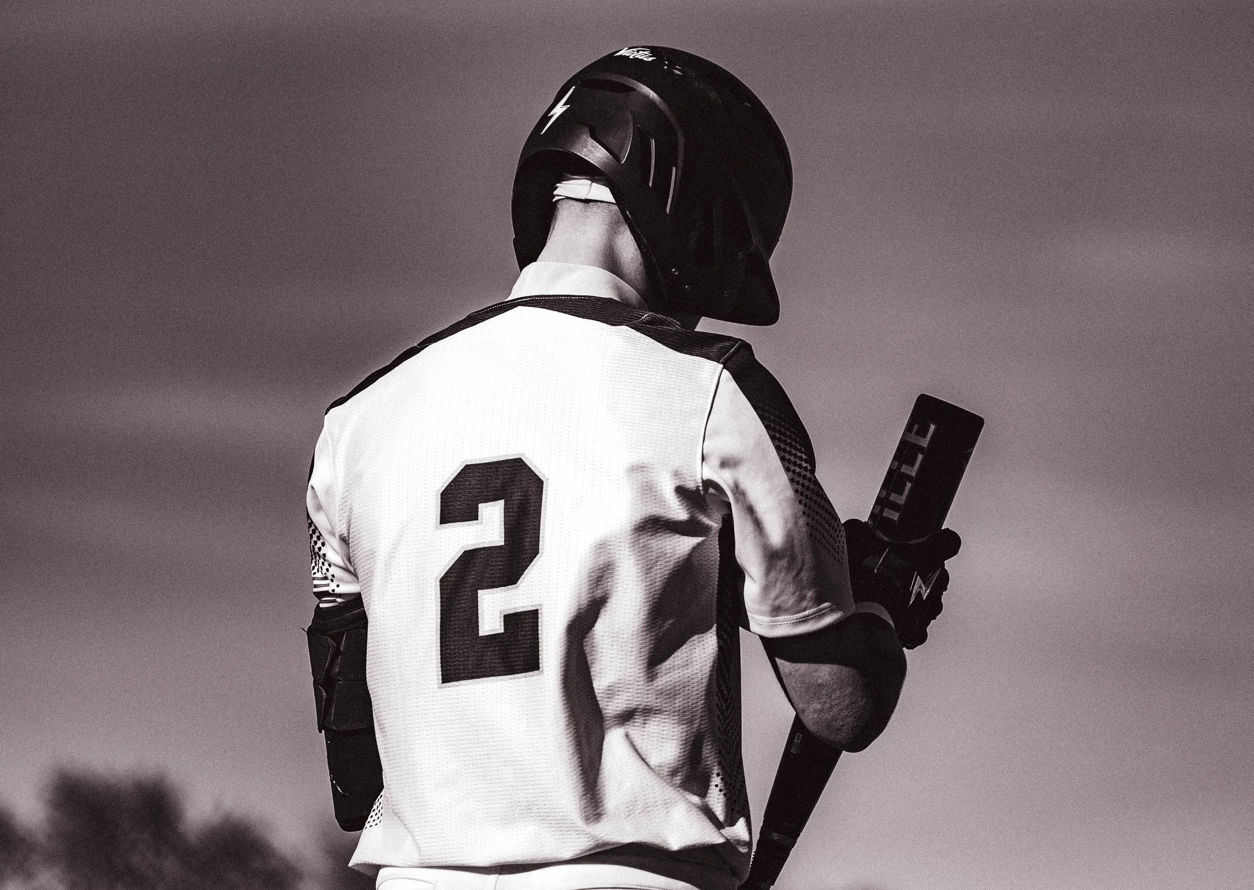 A person wearing a sports helmet and a jersey with the number 2 on the back, holding a hockey stick.