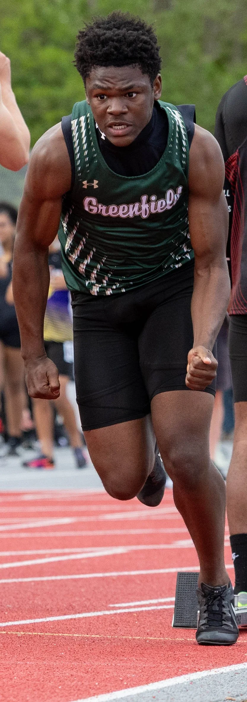 Male athlete in green and black Greenfield jersey sprinting on a track.