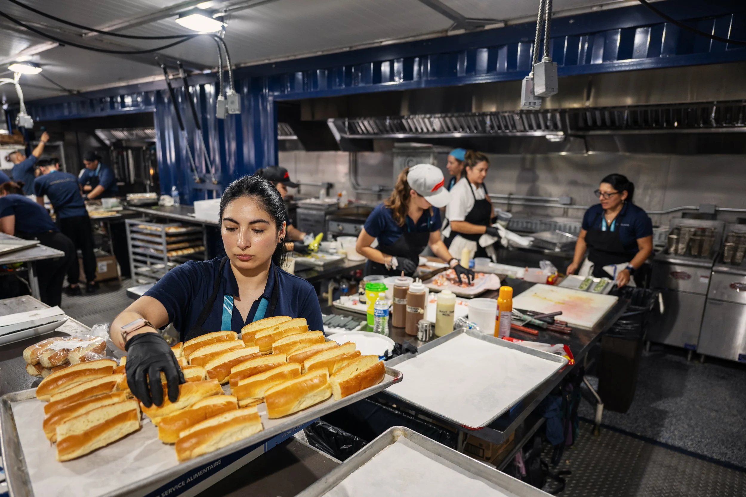 Kitchen staff preparing and packaging gourmet hotdogs in a commercial kitchen.