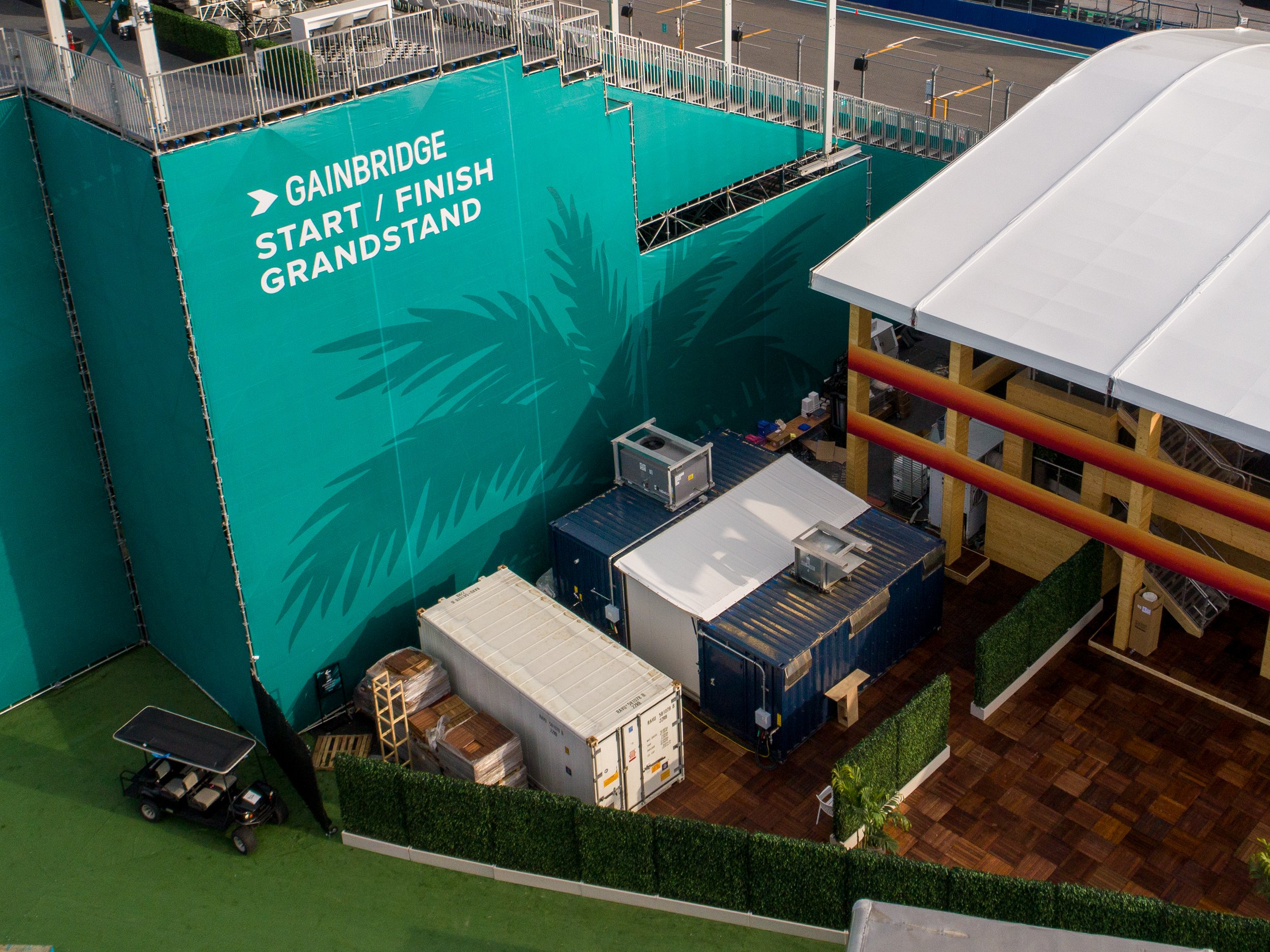 Aerial view of a temporary kitchens with a large teal banner that reads 'GAINBRIDGE START / FINISH GRANDSTAND' and various construction materials, containers, and equipment. It was at the Miami GP formula 1 race.