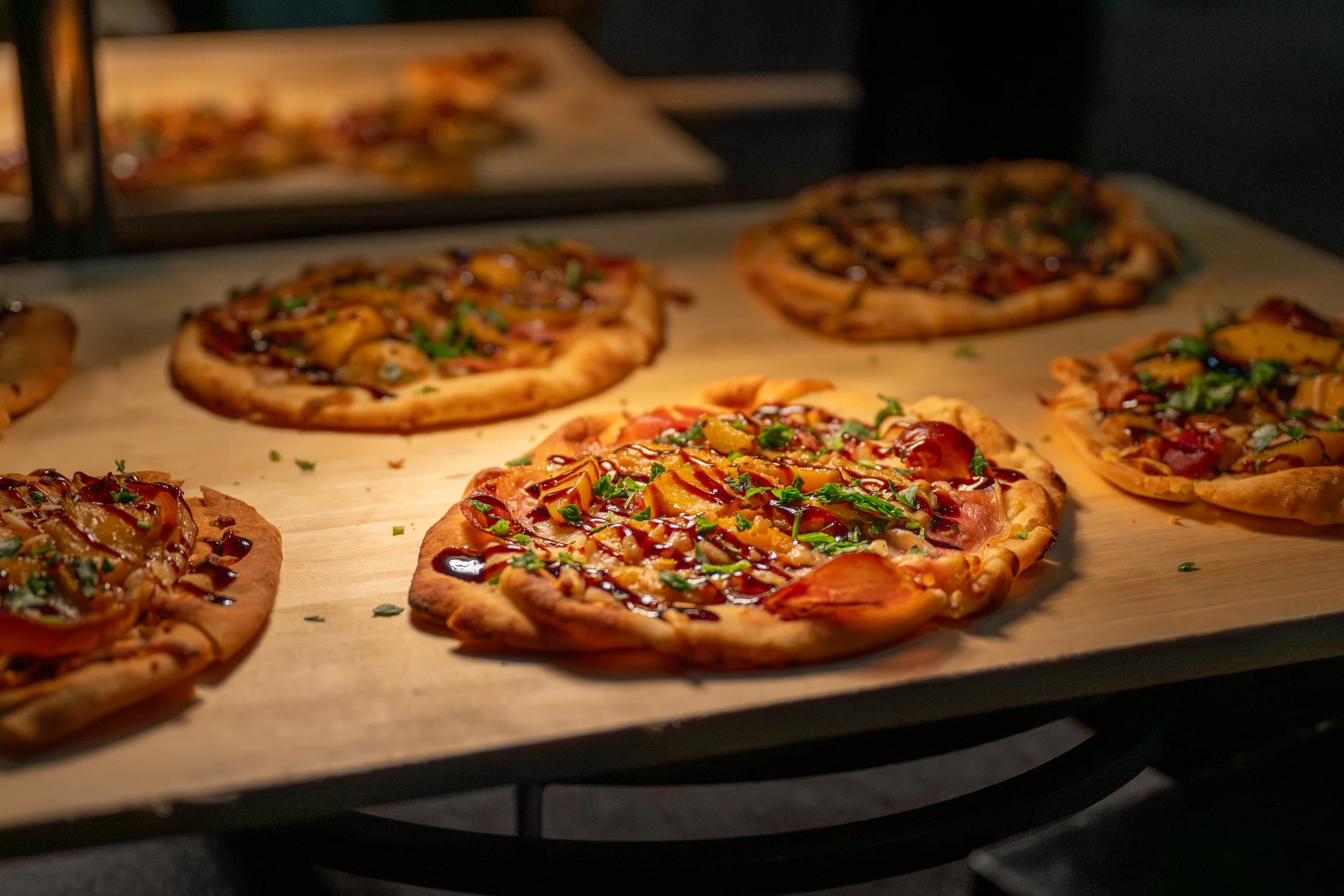 Multiple personal pan pizzas fresh from an oven, with some toppings like vegetables and sauces visible.