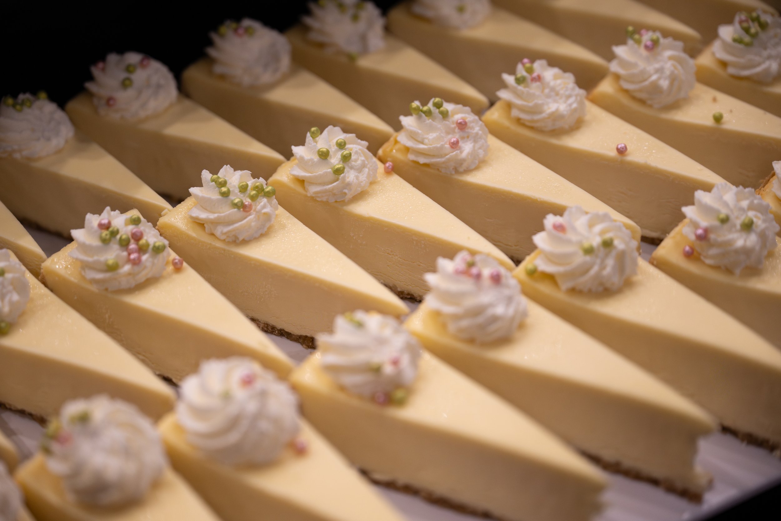 Multiple slices of cheesecake topped with whipped cream and decorated with pink and green edible pearls.