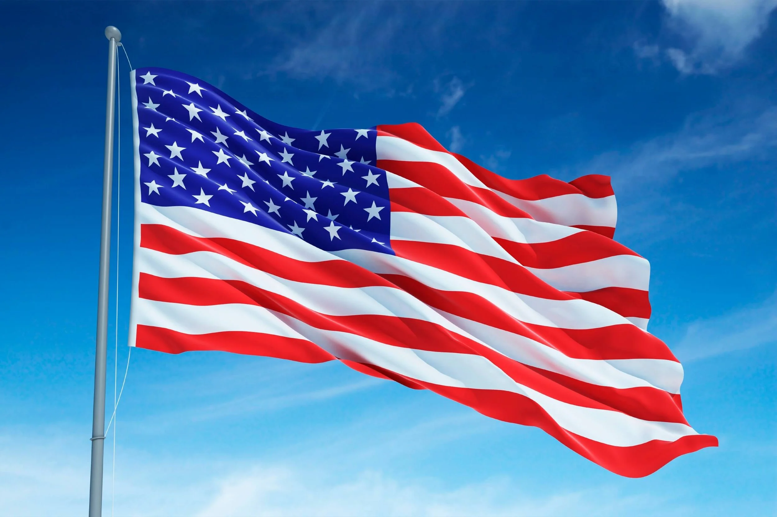 American flag waving in the wind against a blue sky with some clouds.