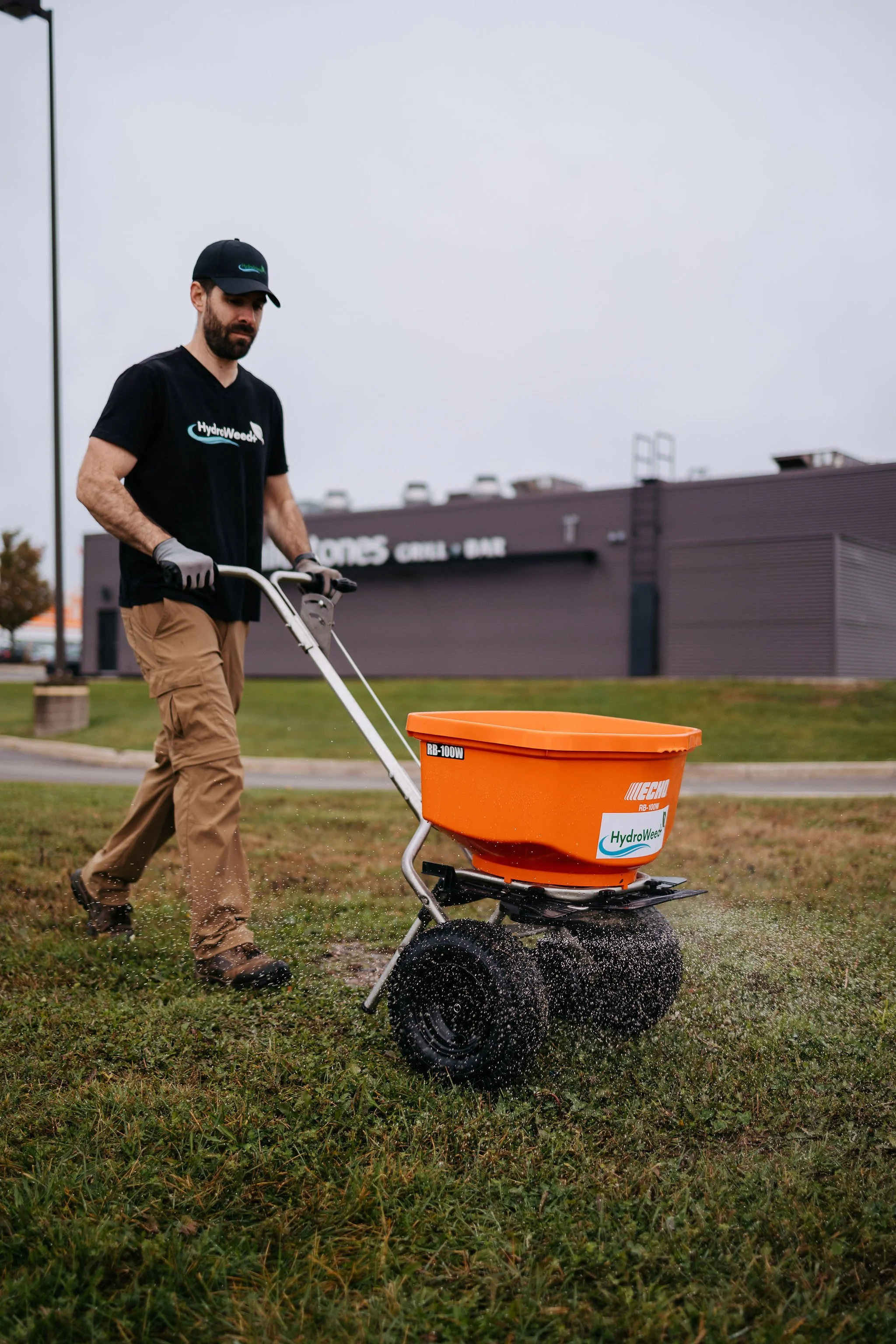 Element Landscape Solutions technician applying lawn care treatment with spreader on commercial property in Moncton, NB