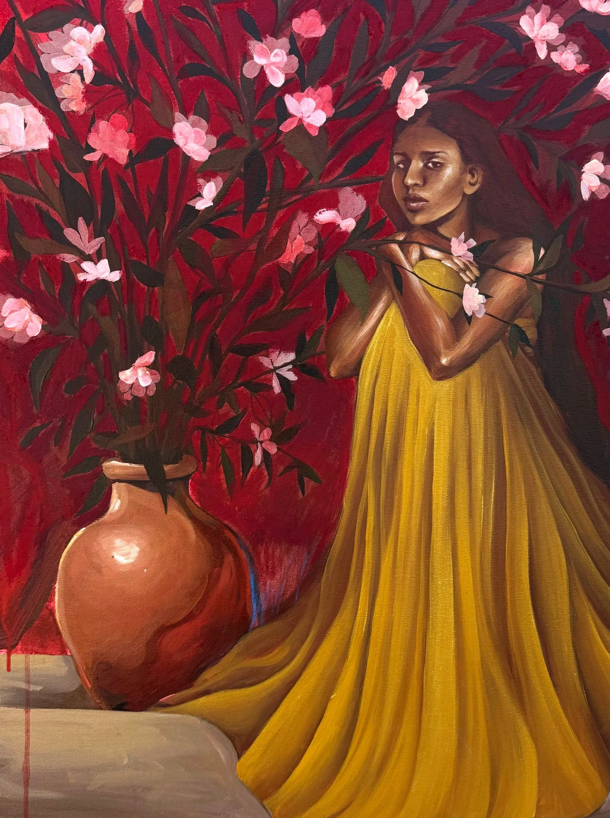A woman with dark skin and long hair holding a branch with pink flowers, wearing a yellow dress, standing in front of a large red background.