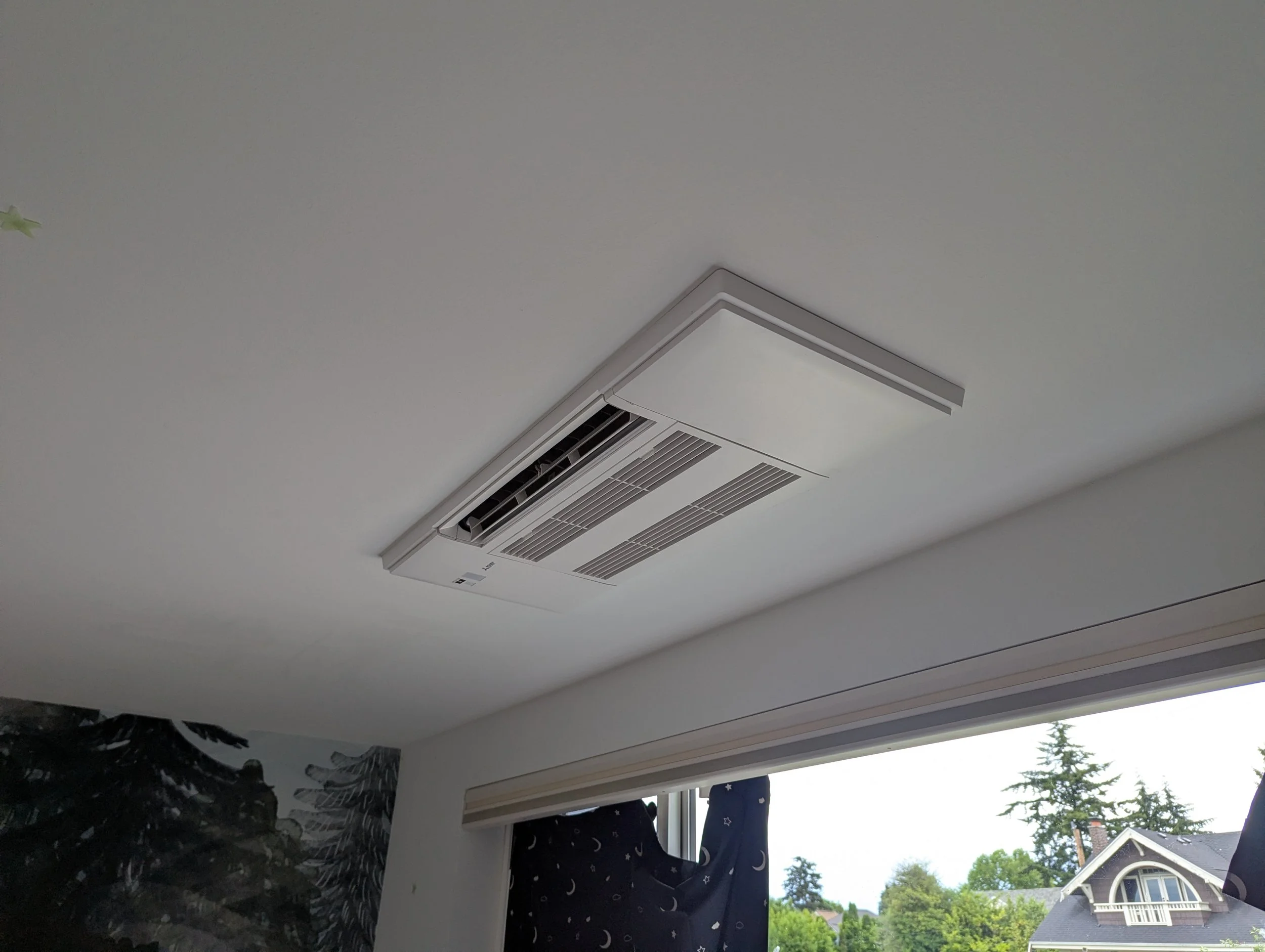 View of a in-ceiling (recessed), air conditioning vent, next to a window with outdoor trees and houses.
