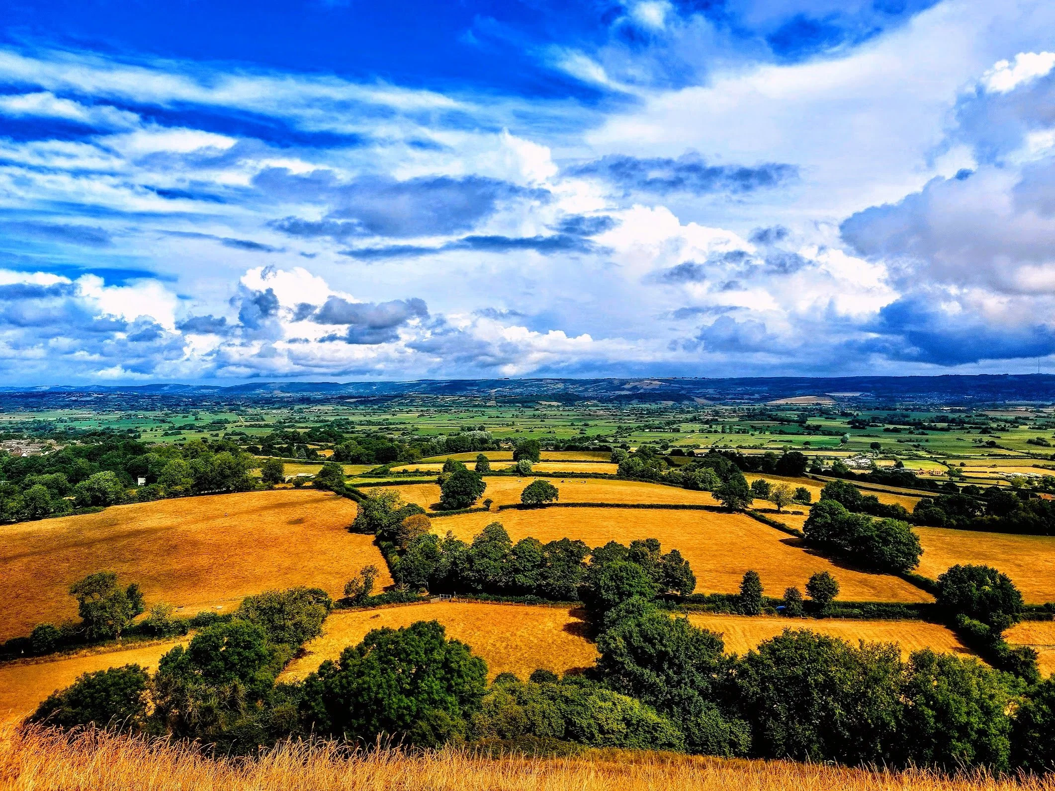 A view across the English countryside where the fields form a patchwork across the landscape beneath a wide dramatic sky.